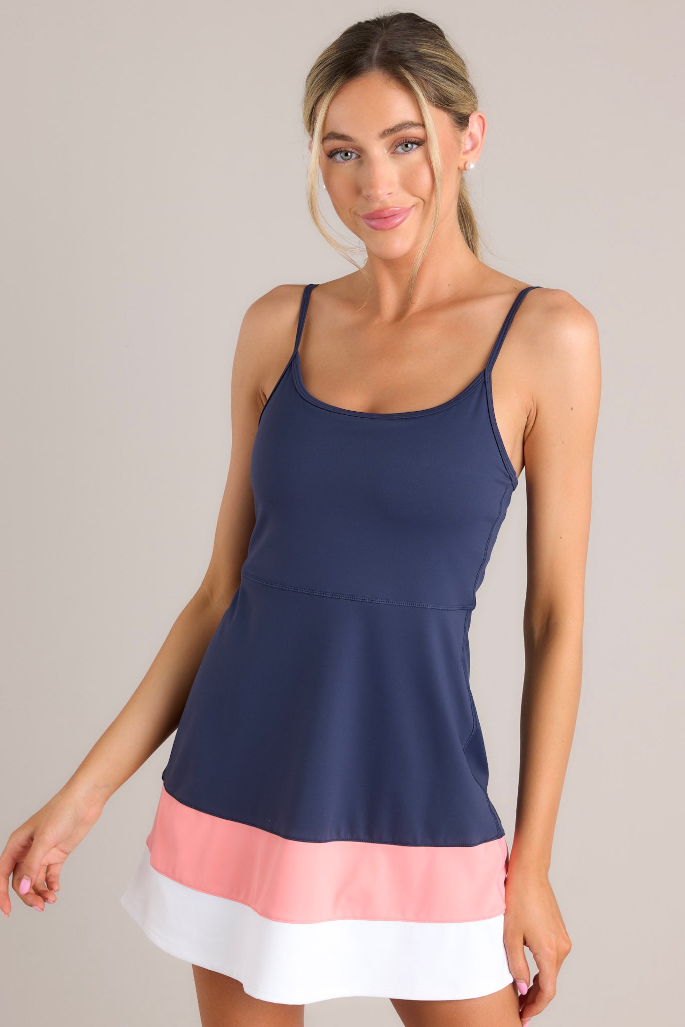 Angled front view of this dress that features a rounded neckline, thin adjustable straps, a built-in shelf bra, built-in shorts with functional pockets, and a color blocked hemline.