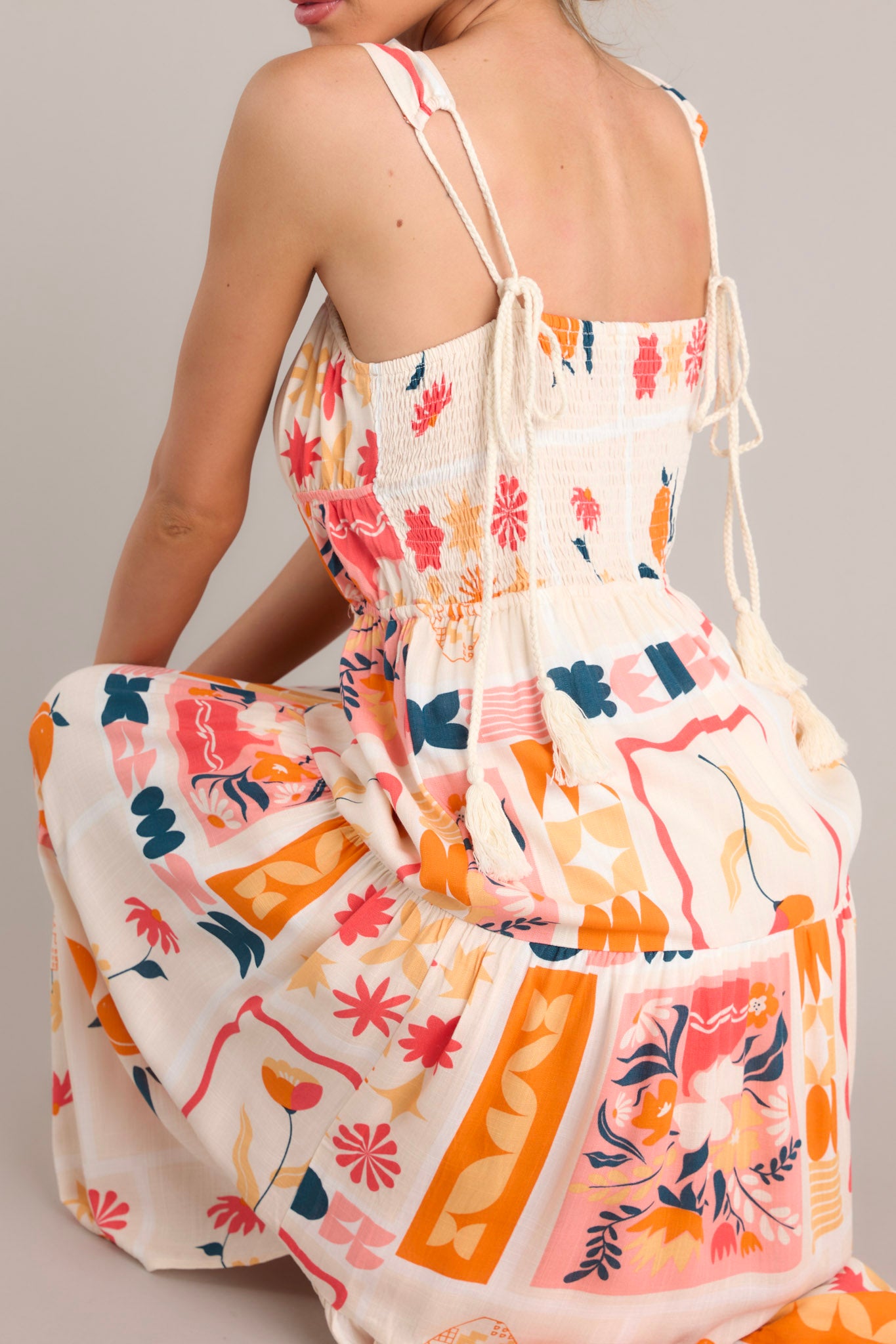 Back view of multi patterned dress featuring a smocked insert in the back of the bust, adjustable tassel ties, and an elastic waist.