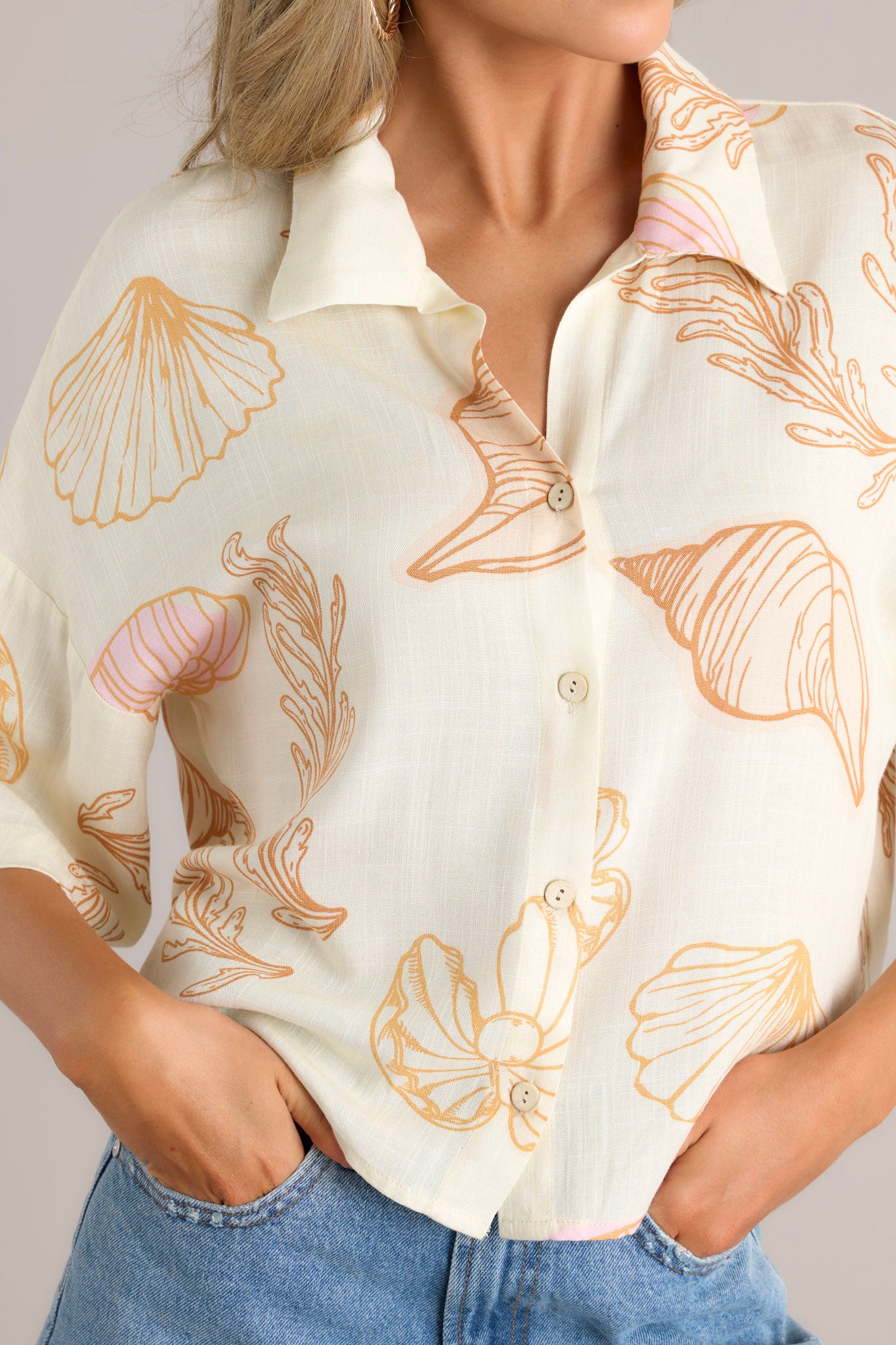 Close up view of this ivory top featuring a collared neckline, a seashell print on lightweight fabric, and a slightly cropped length.