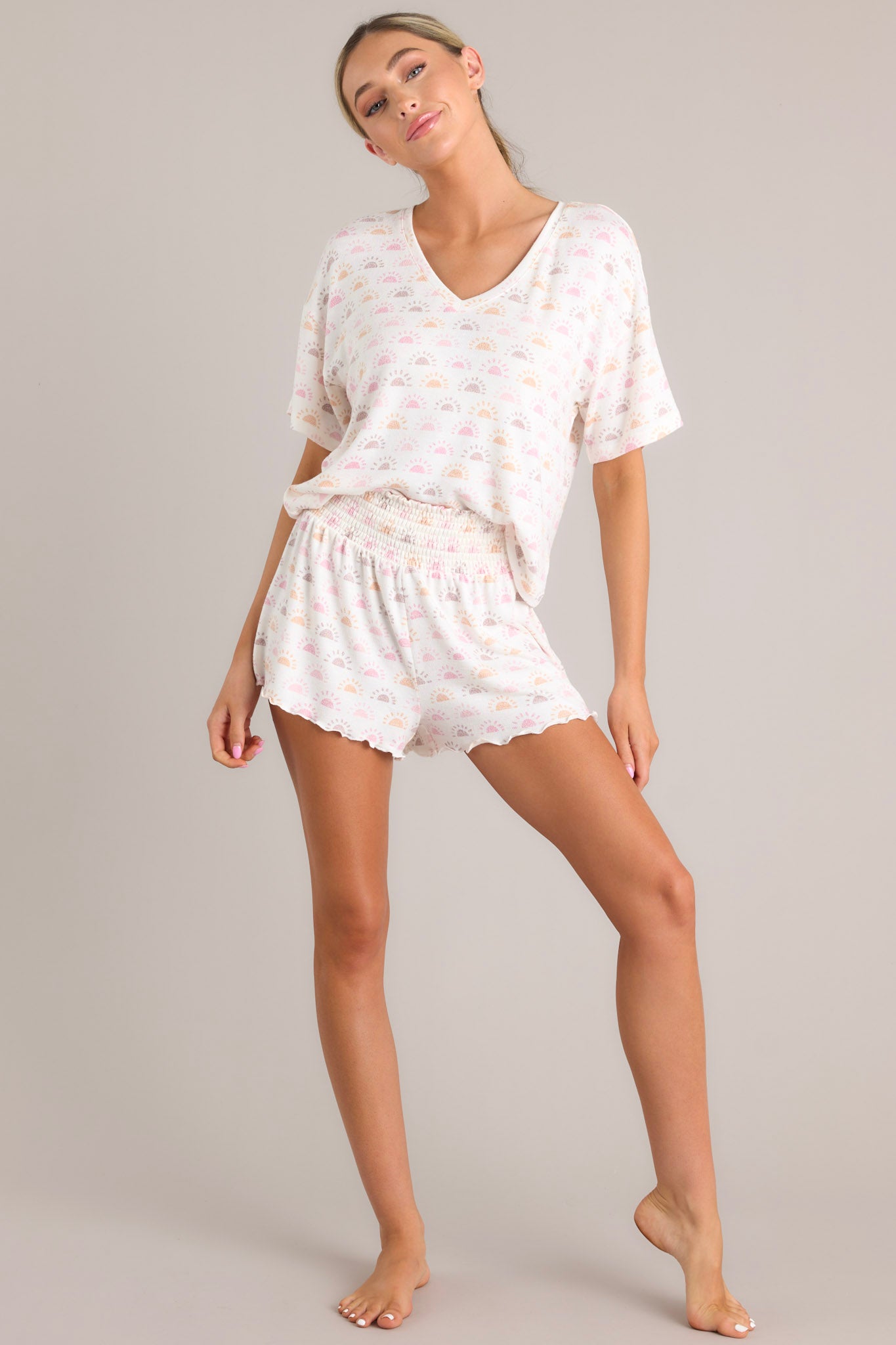 Full view of these white shorts featuring a smocked elastic waistband, lettuce hemline, and lightweight sun print.