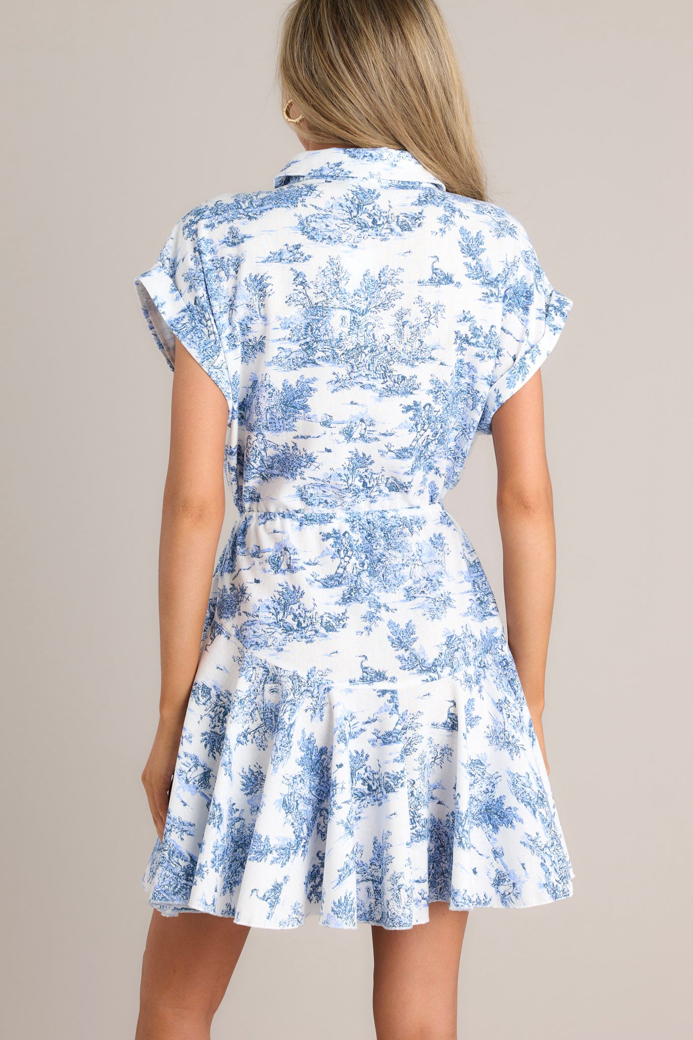 Back view of this dress that features a collared neckline, functional buttons, a self-tie waist feature, a flowy skirt, and wide cuffed short sleeves.