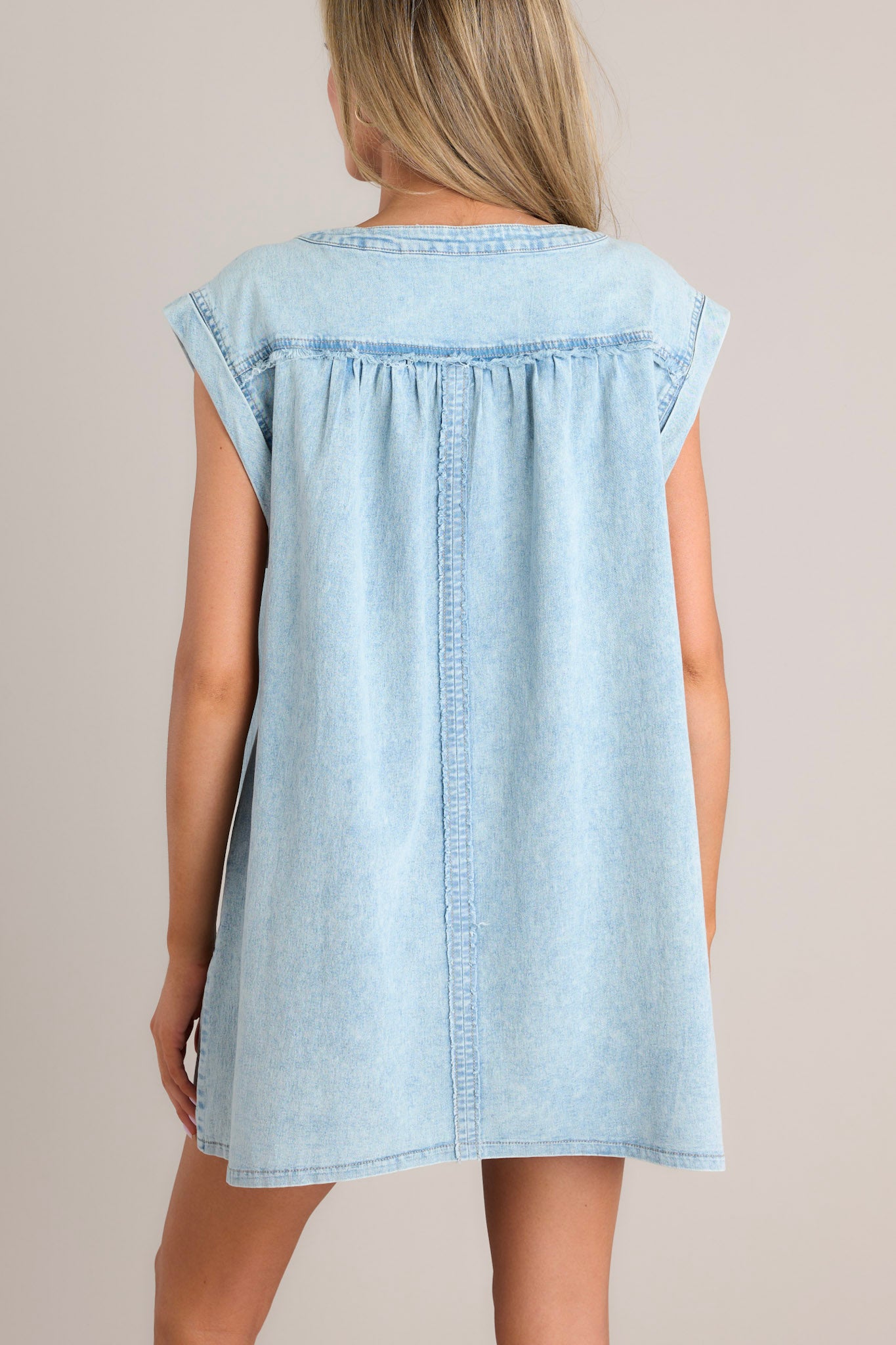 Back view of this dress that features a v-neckline, a self-tie feature, gathering in the bust, a thick seam down the front and back, functional hip pockets, and wide cuffed short sleeves.