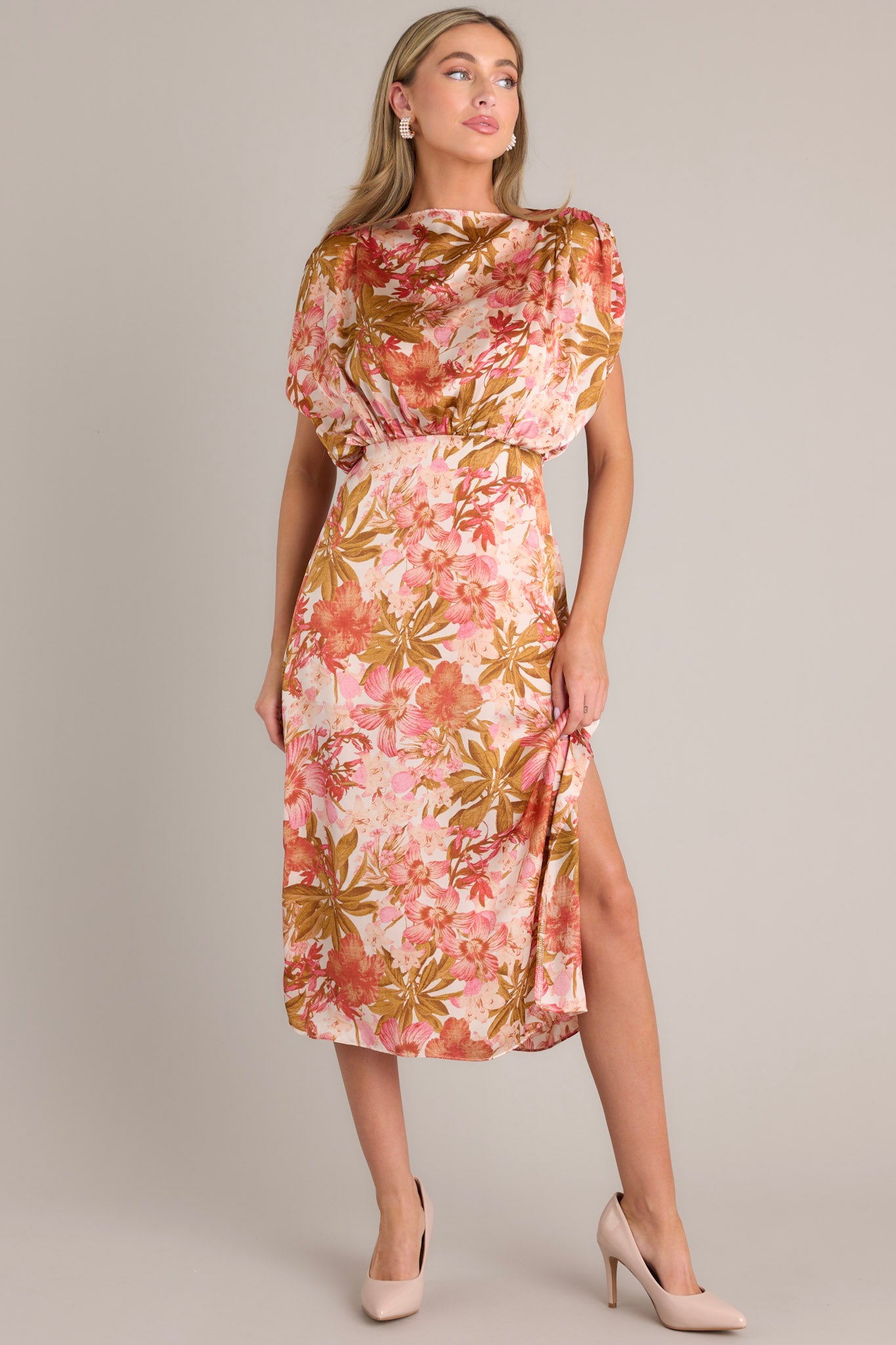 Full body angled view of this knee-length rose pink dress with a boat neckline, gathered waist, elastic insert in the back, discreet side zipper, side slit, and wide sleeves.