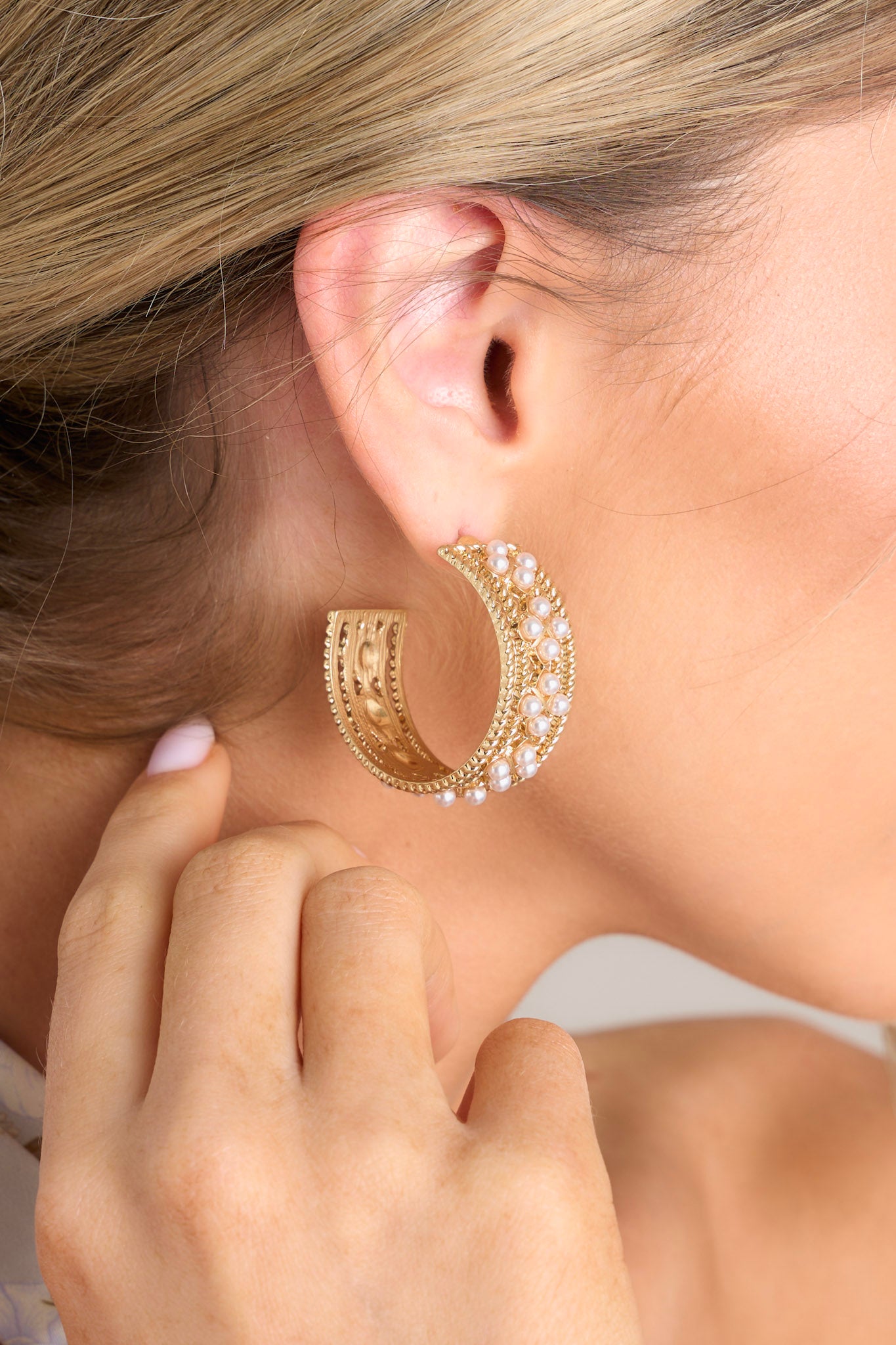 Side view of these hoops that feature gold hardware, faux pearl embellishments, and secure post backings.