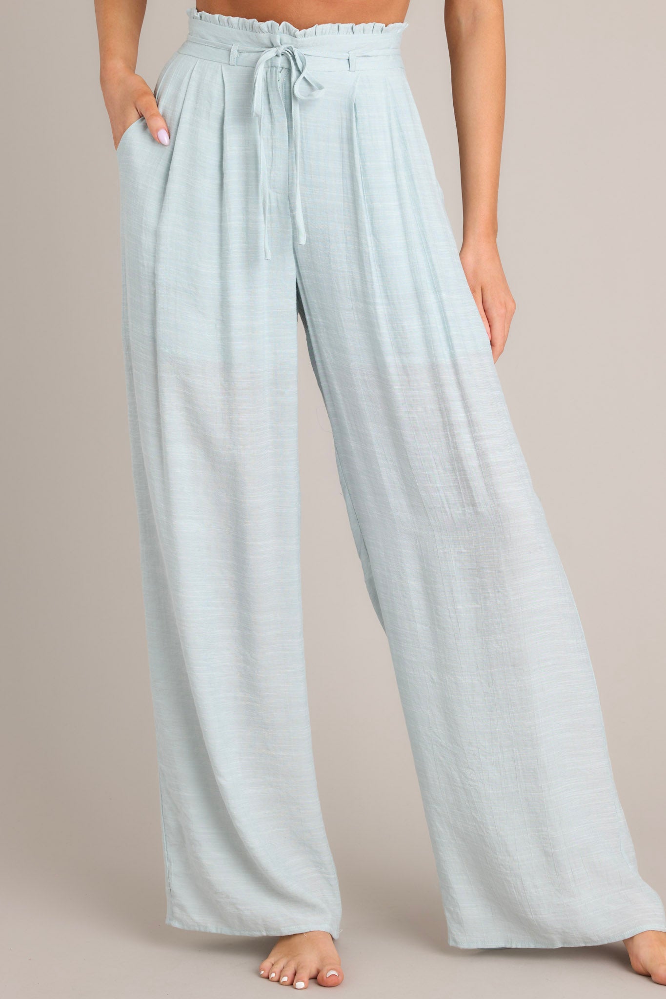 Front view of these pants that feature a high waisted design, a self-tie closure that doubles as a belt, belt loops, functional hip pockets, a lightweight fabric, and a wide leg.