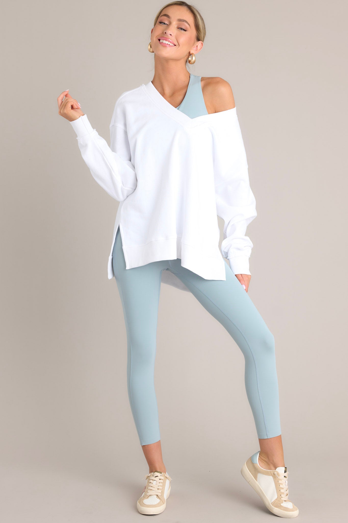 This white sweatshirt features a v-neckline, a soft material, a split hemline, and ribbed cuffed sleeves.