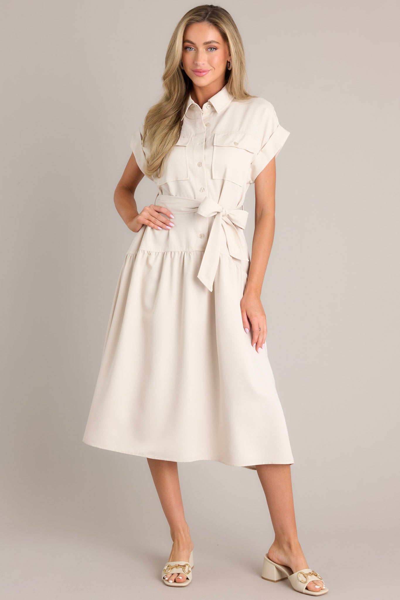 Front view of this beige dress that features a collared neckline, functional breast pockets, a button front, a self-tie belt, belt loops, functional hip pockets, a single tier, and cuffed short sleeves.