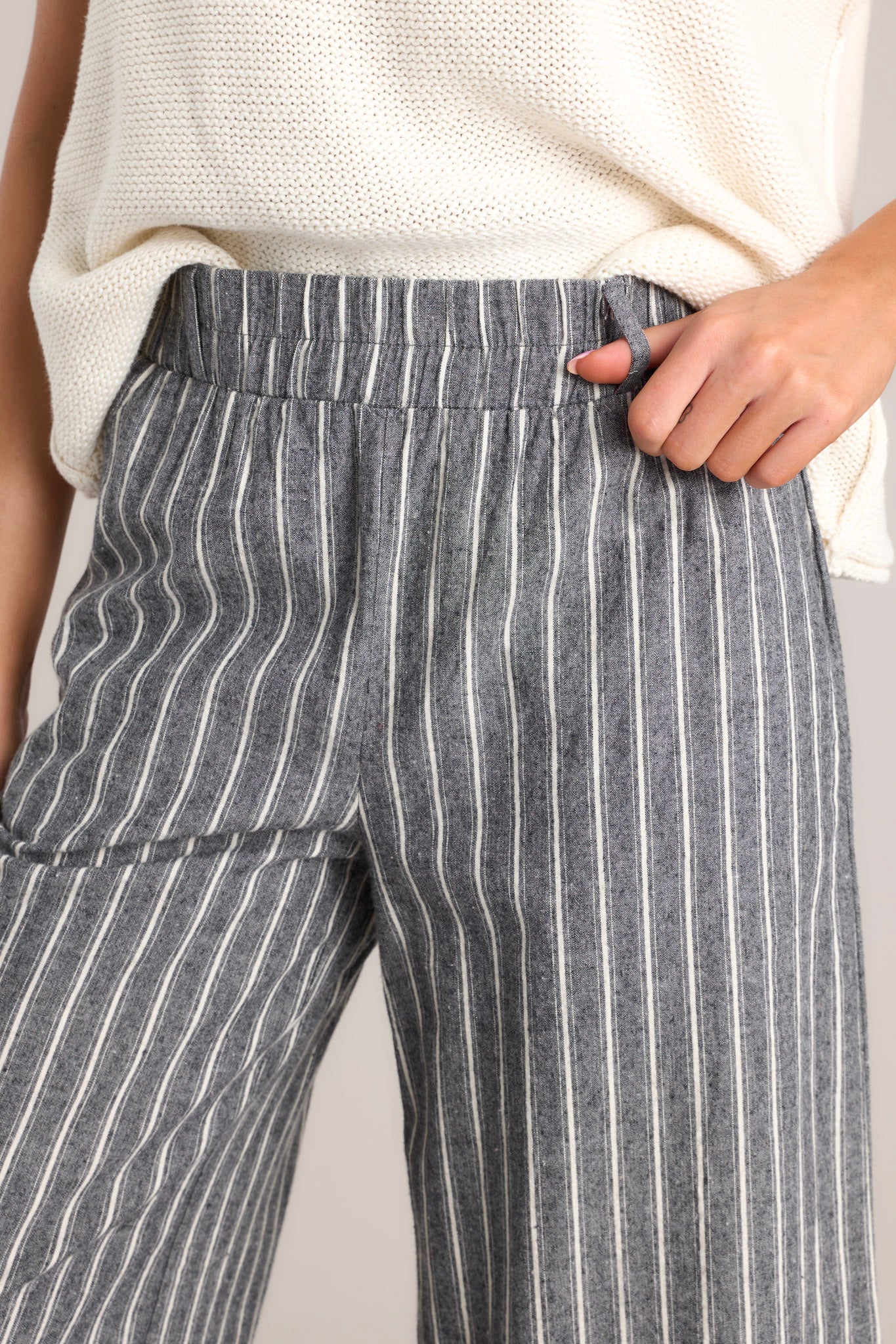 Close-up of the high rise, elastic waistband, belt loops, optional self-tie belt, and the fabric texture of the charcoal striped pants.