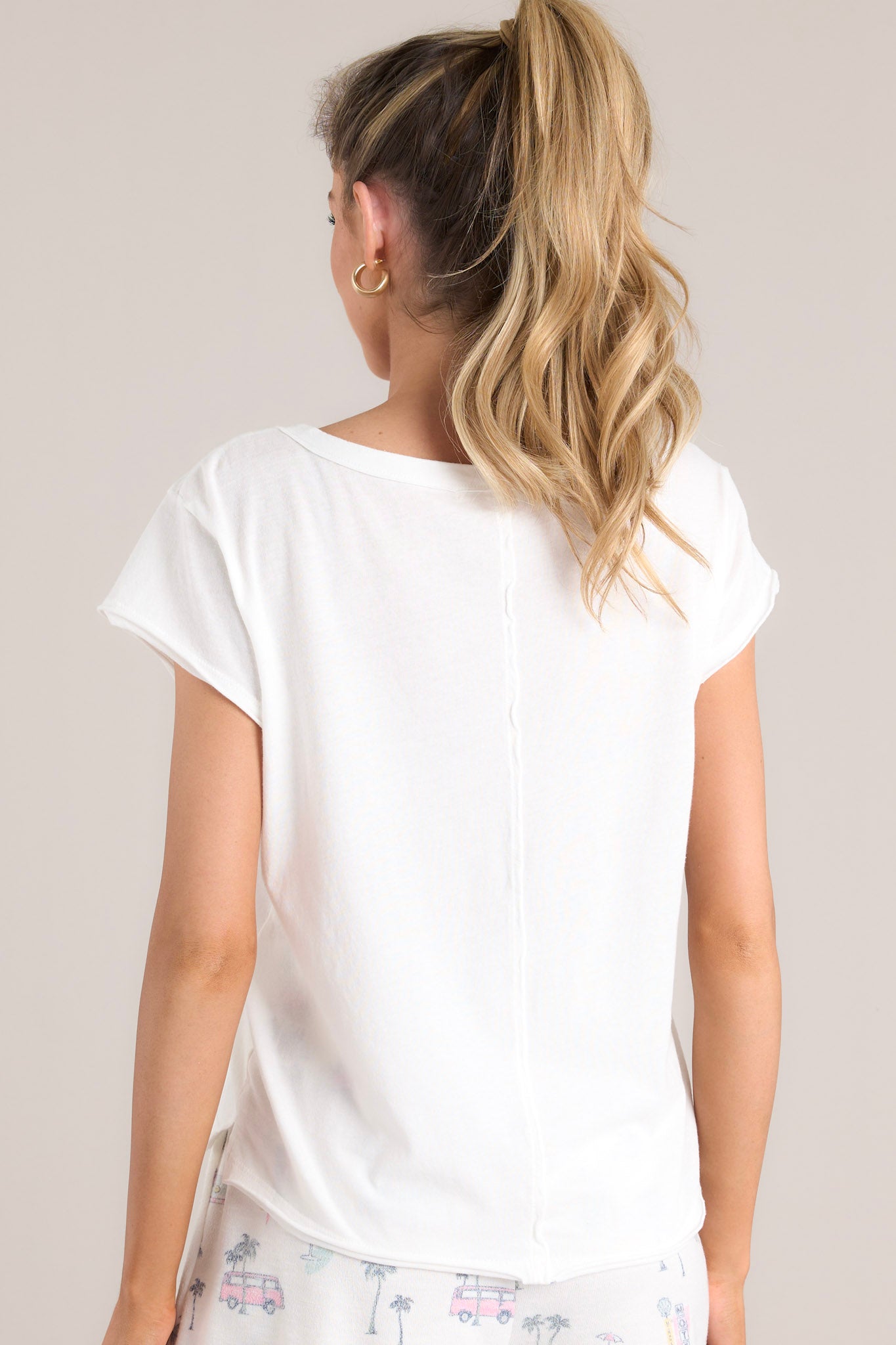 Back view of this tee that features a crew neckline, a vacation themed graphic, a light & airy material, a slightly cropped length, a split hemline, and short sleeves.