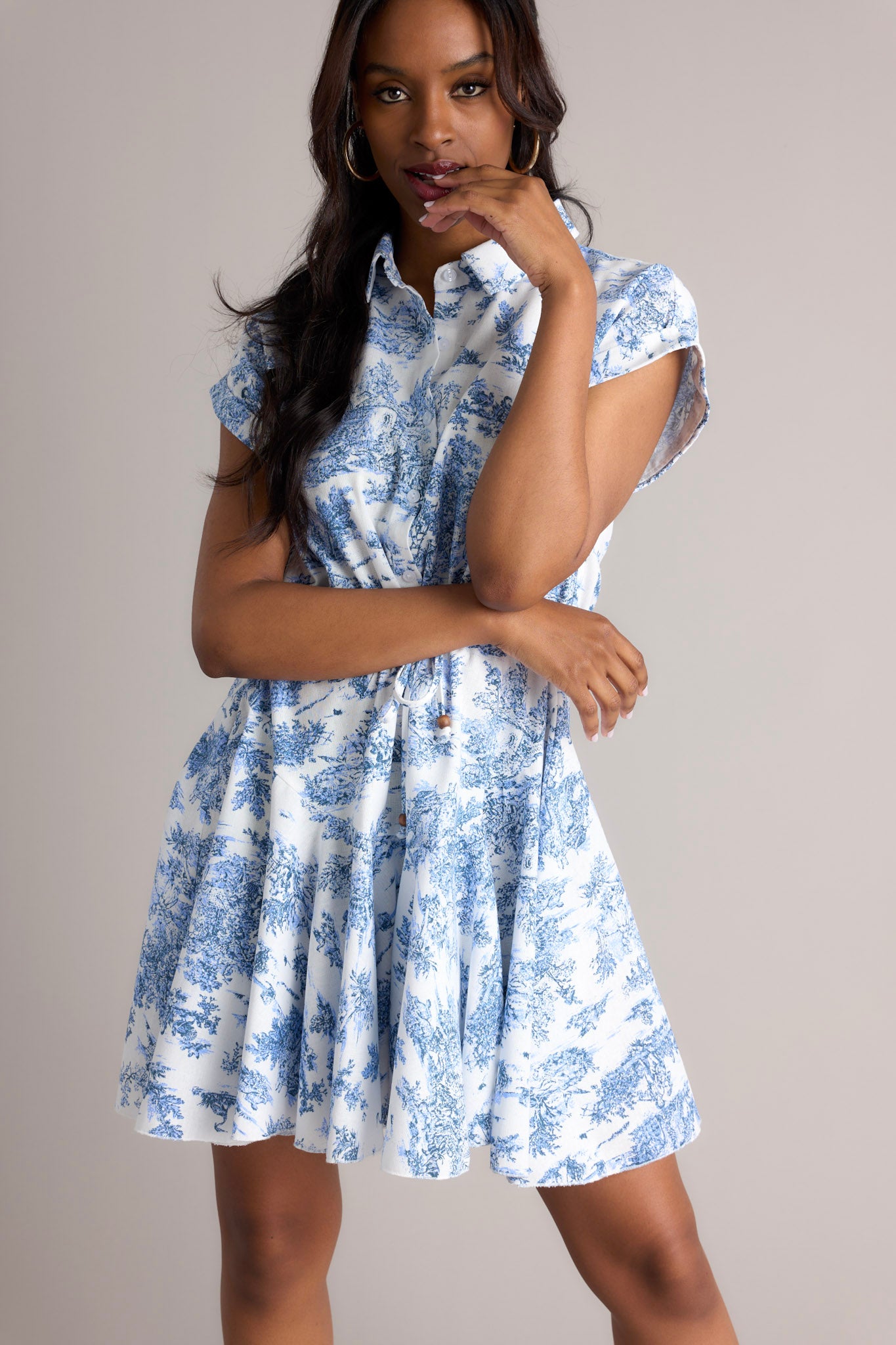 This white and blue dress features a collared neckline, functional buttons, a self-tie waist feature, a flowy skirt, and wide cuffed short sleeves.