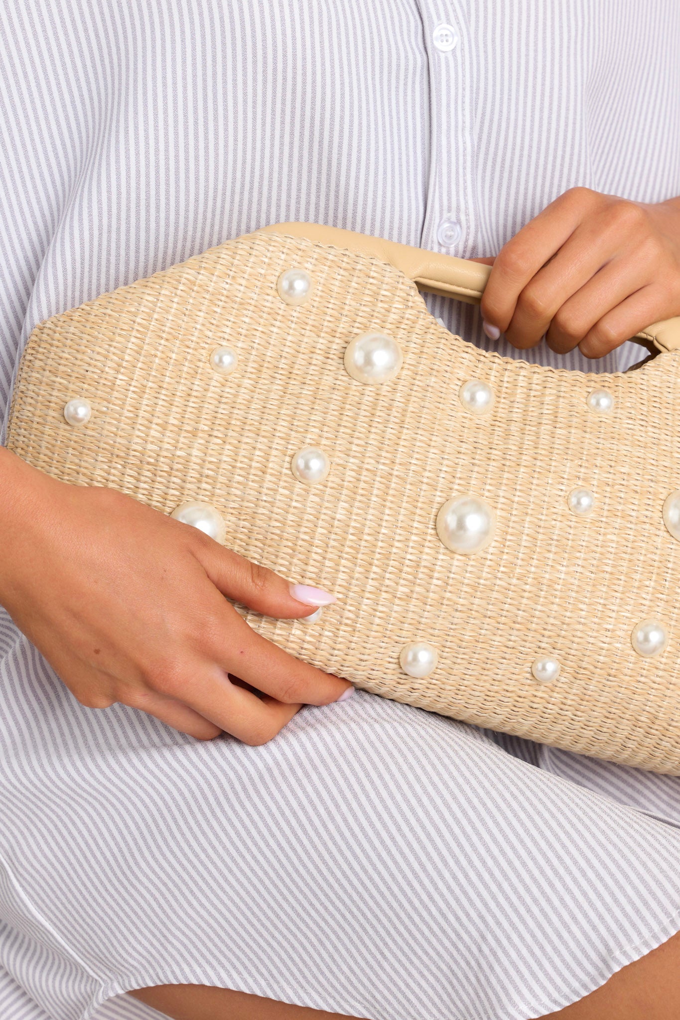 Close up view of this clutch that features a hinged closure, faux leather handles, a rattan material, faux pearl embellishments, and a zipper pocket inside.