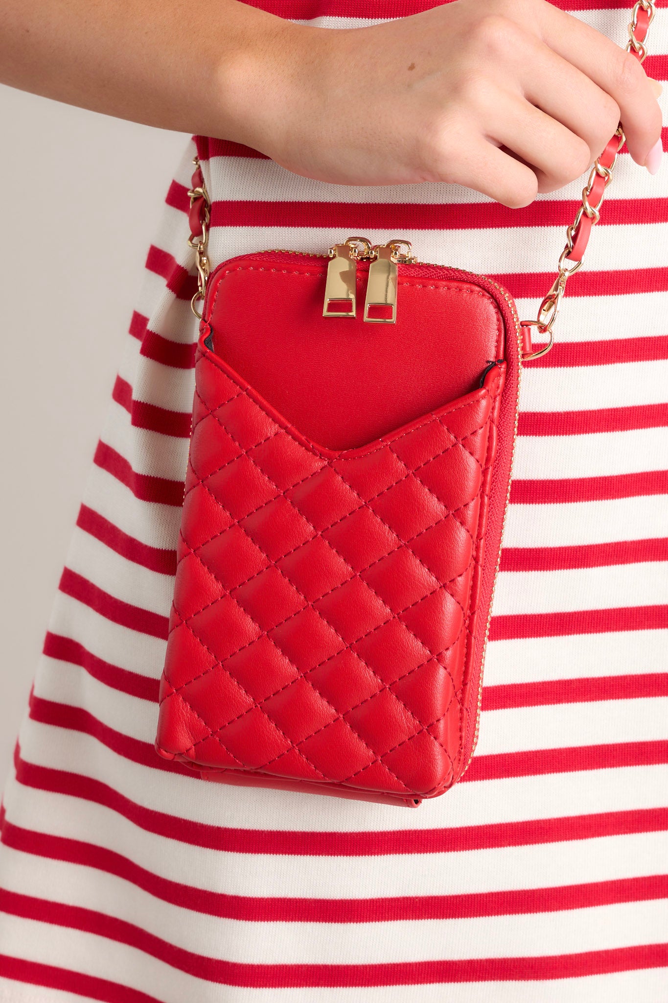 Close up view of this red bag that features gold hardware, a removable chain strap, a phone pocket, and multiple pockets inside.