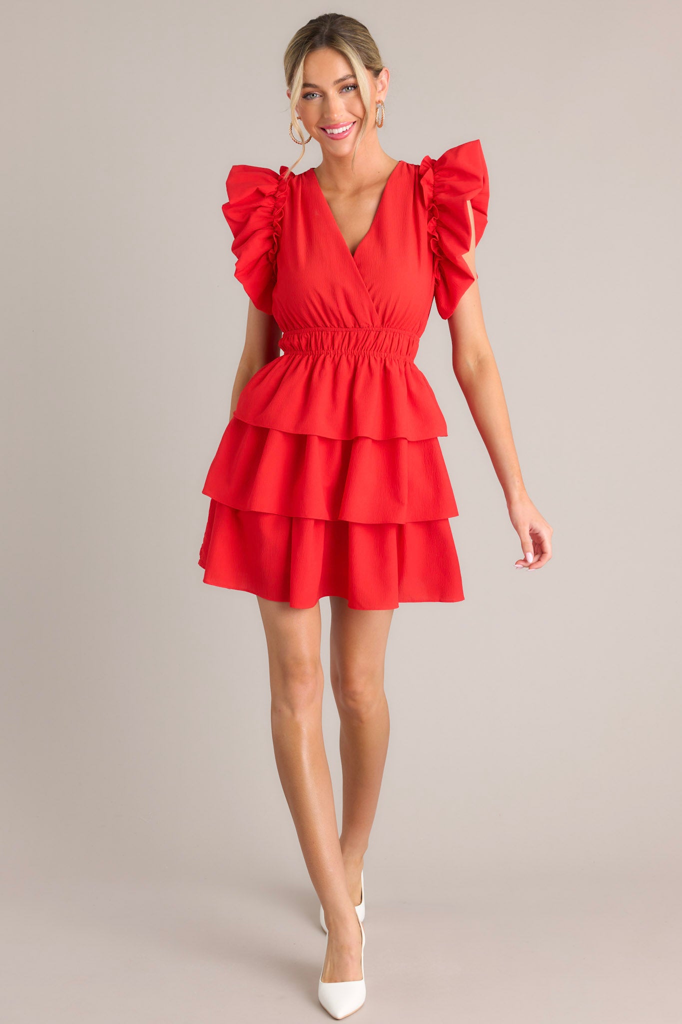 Front view of this red mini dress that features a v-neckline, an elastic waist, a tiered design, and short flutter sleeves.