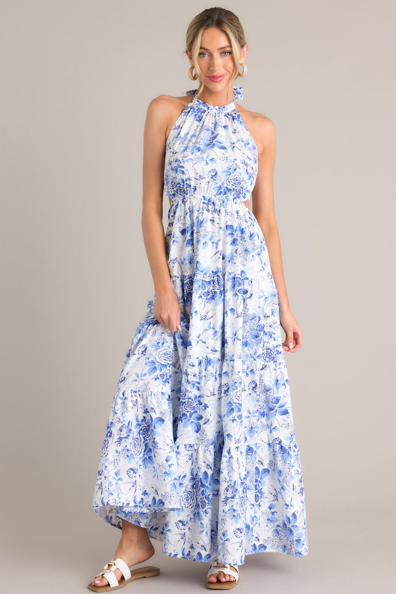 Front view of this floral maxi dress that features a self-tie halter neckline, an open back, a self-tie back feature, an elastic waistband, side cutouts, and a tiered design.