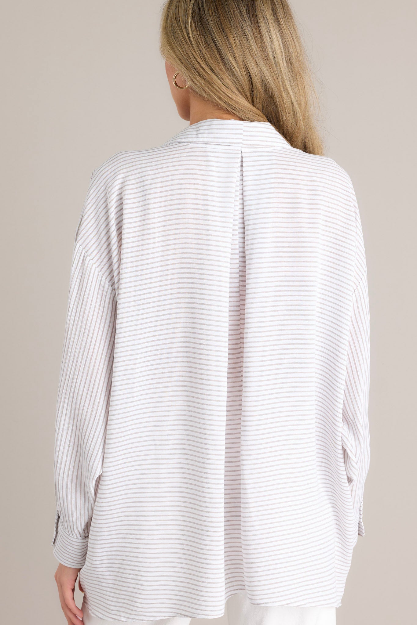 Back view of this white stripe top that features a collared neckline, a functional button front, a breast pocket, a unique stripe pattern going both vertically & horizontally, button cuffed long sleeves, and a split hemline.