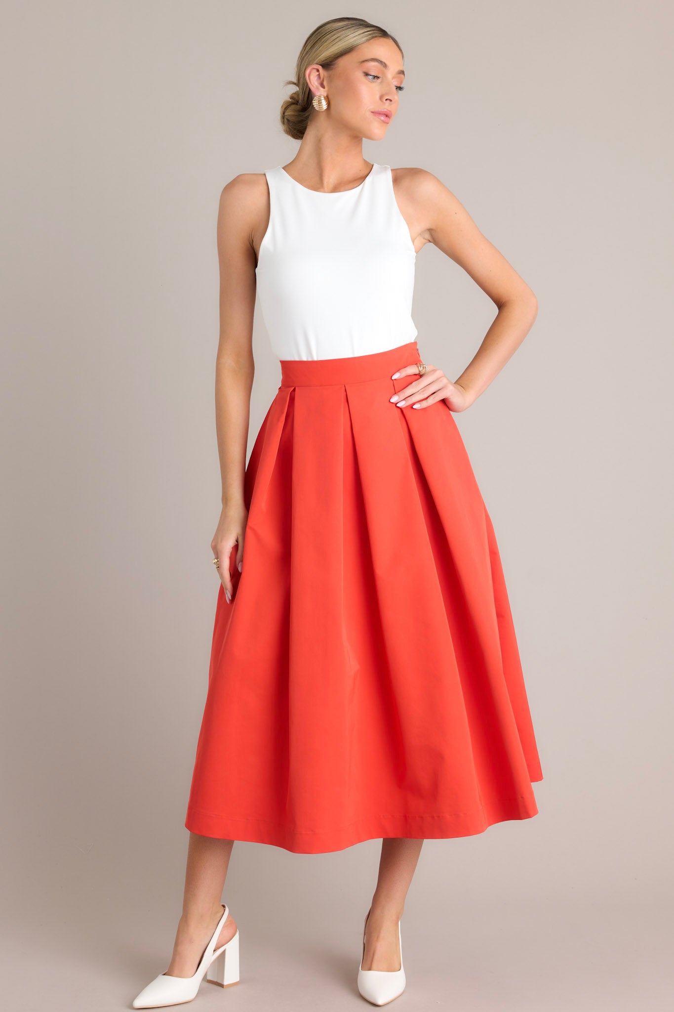 Angled full body view of this tomato red midi skirt that features a high waisted design, a discrete side zipper, a thick waistline and functional pockets.