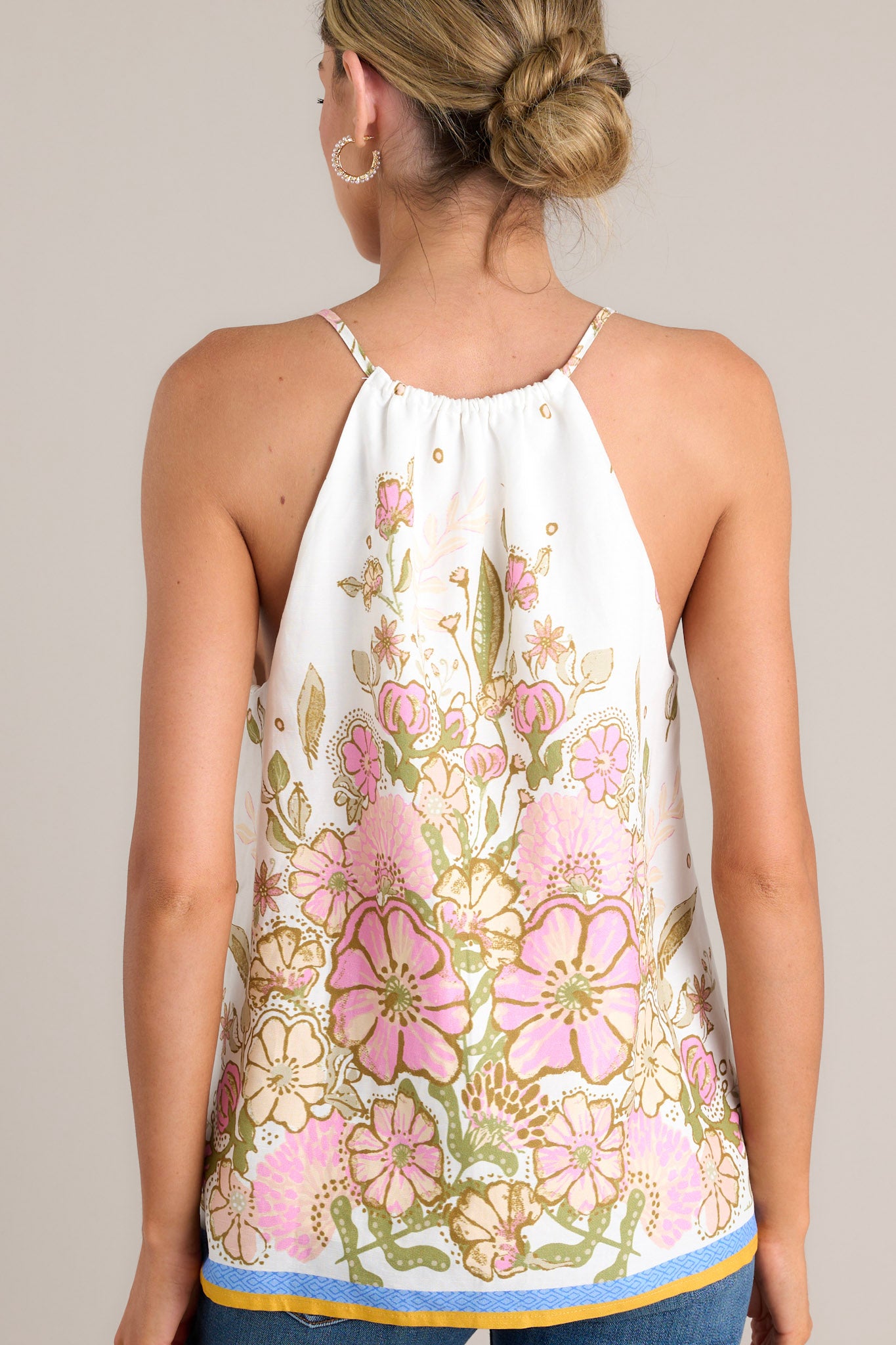 Back view of this  ivory tank top with a v-neckline featuring a self-tie feature, thin straps, a faux button front, and a unique floral pattern.