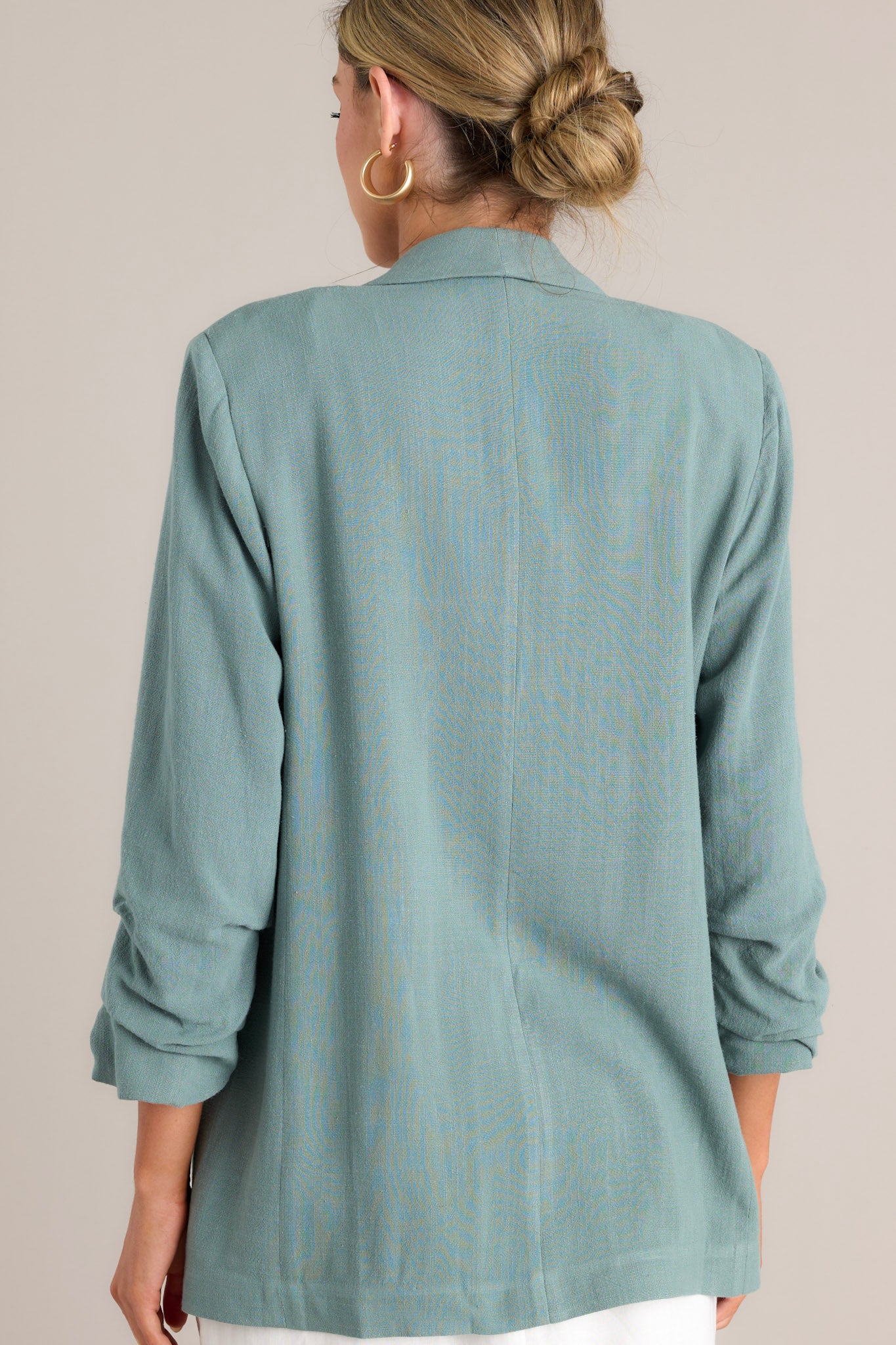 Back view of this forest green blazer with a folded neckline, shoulder padding, faux pockets, and gathered quarter-length sleeves.