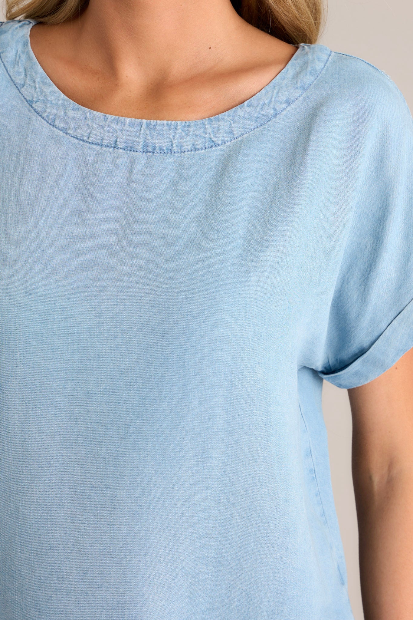 Close up view of this light chambray top that features a crew neckline, a relaxed fit, and a wide cuffed short sleeves.