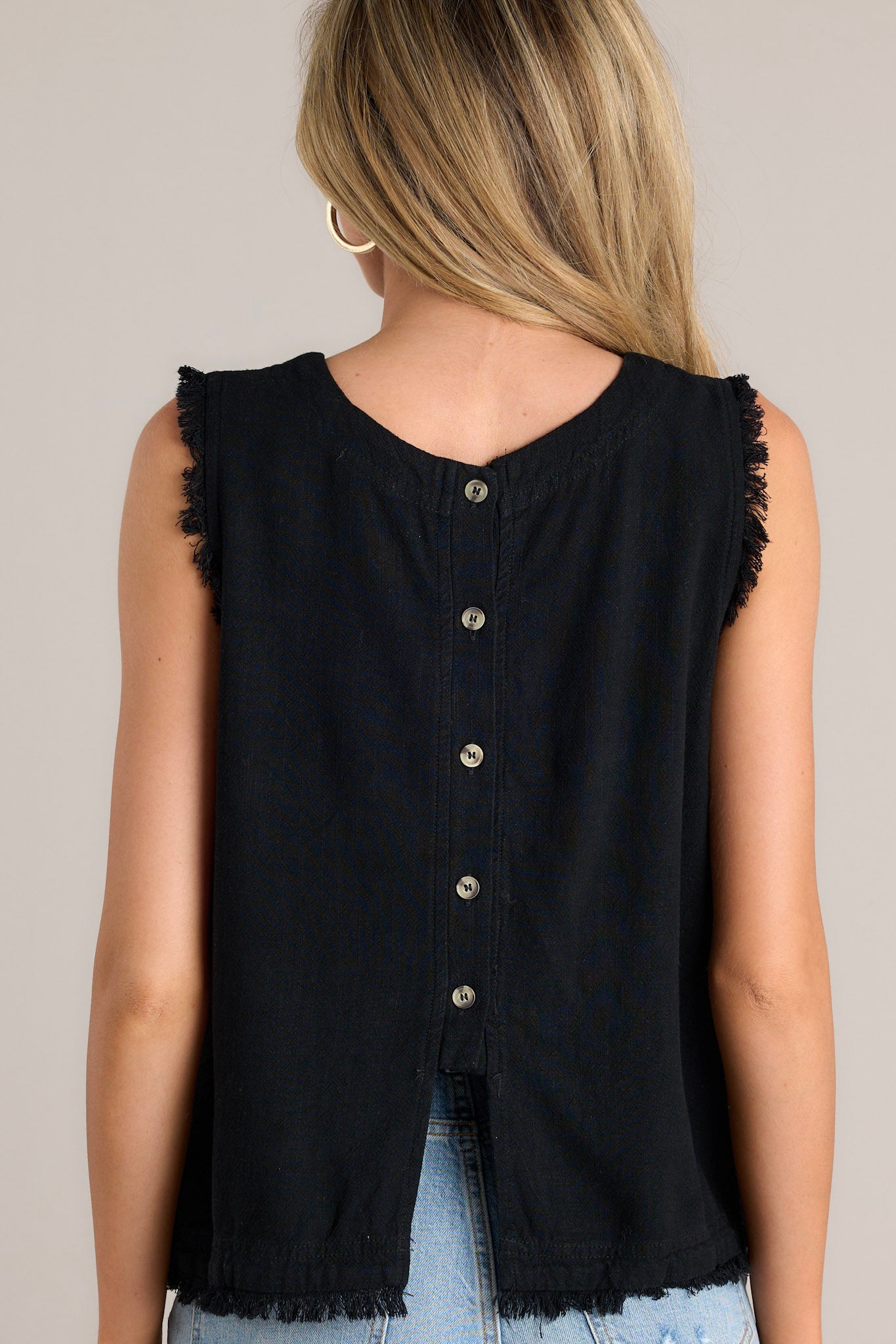 Back view of this black tank that features a crew neckline, functional buttons down the back, frayed shoulders, and a frayed hemline.