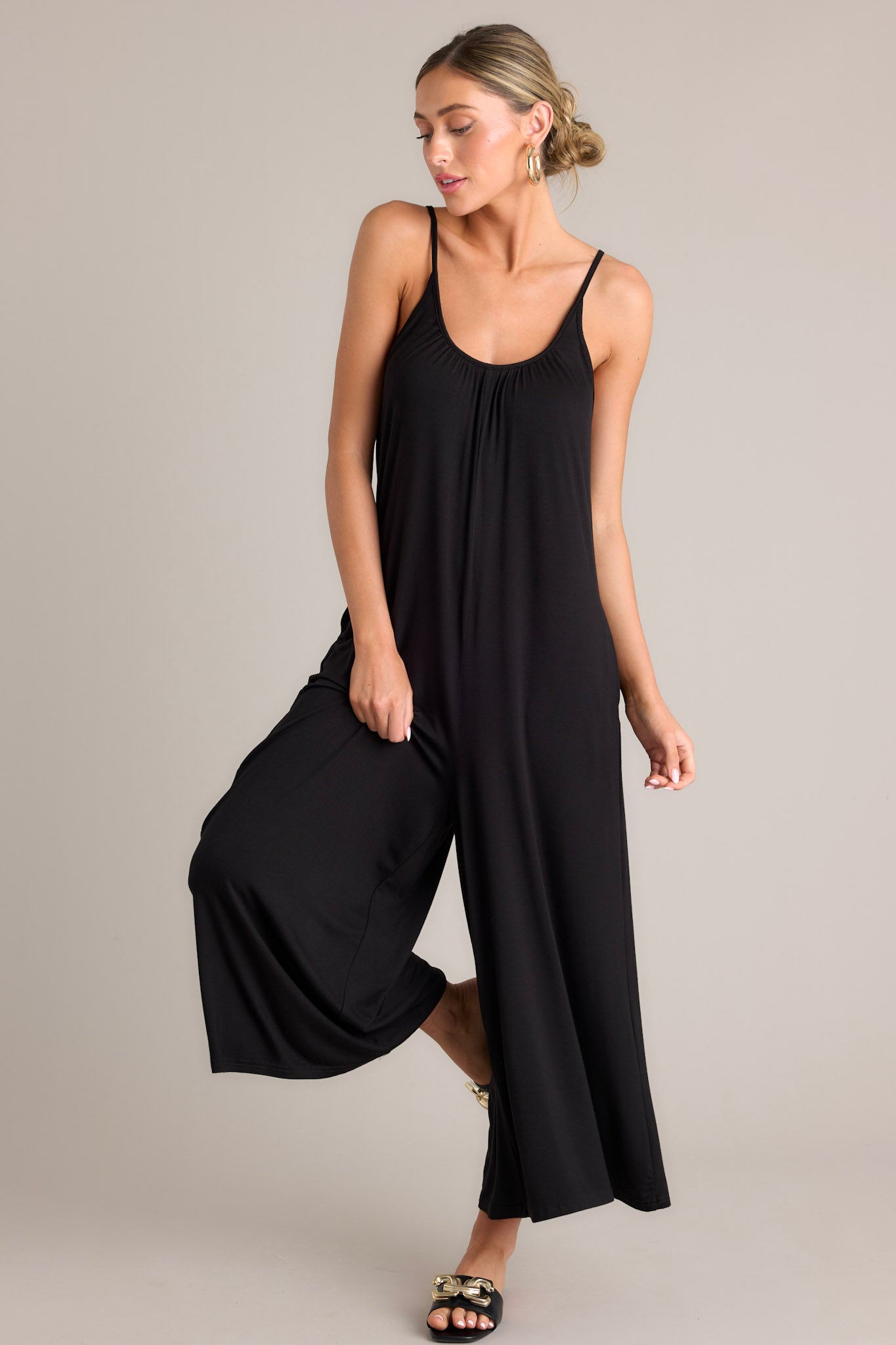 This black jumpsuit features a scoop neckline, thin adjustable straps, an open back, a relaxed fit, functional hip pockets, and a wide leg.