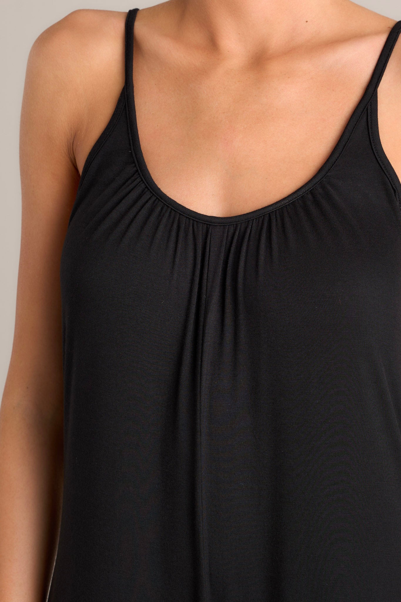 Close up view of this black jumpsuit that features a scoop neckline, thin adjustable straps, an open back, a relaxed fit, functional hip pockets, and a wide leg.