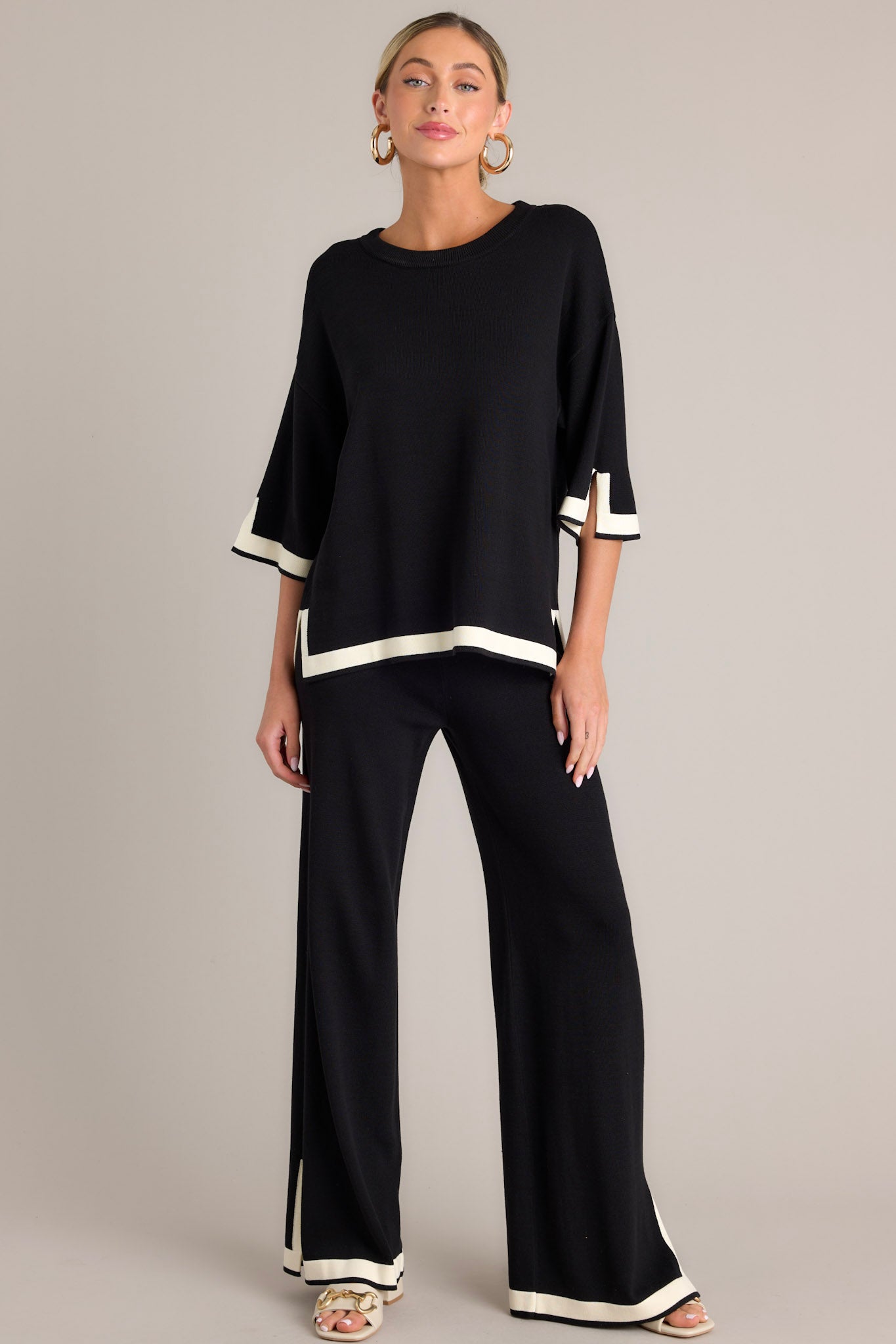 Full body view of this black sweater top that features a crew neckline, a relaxed fit, split quarter sleeves, and contrasting split hemlines.