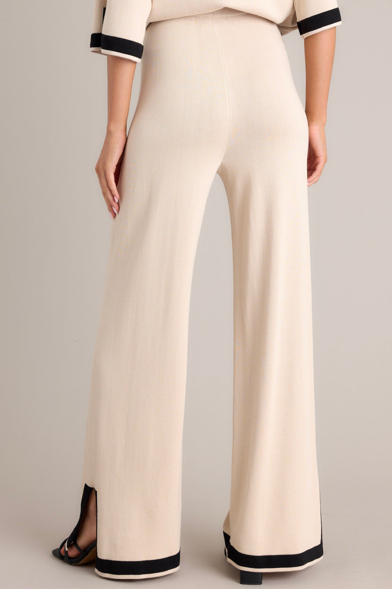 Back view of these beige sweater pants that feature a high waisted design, an elastic waistband, a wide leg, and a contrasting split hemline.