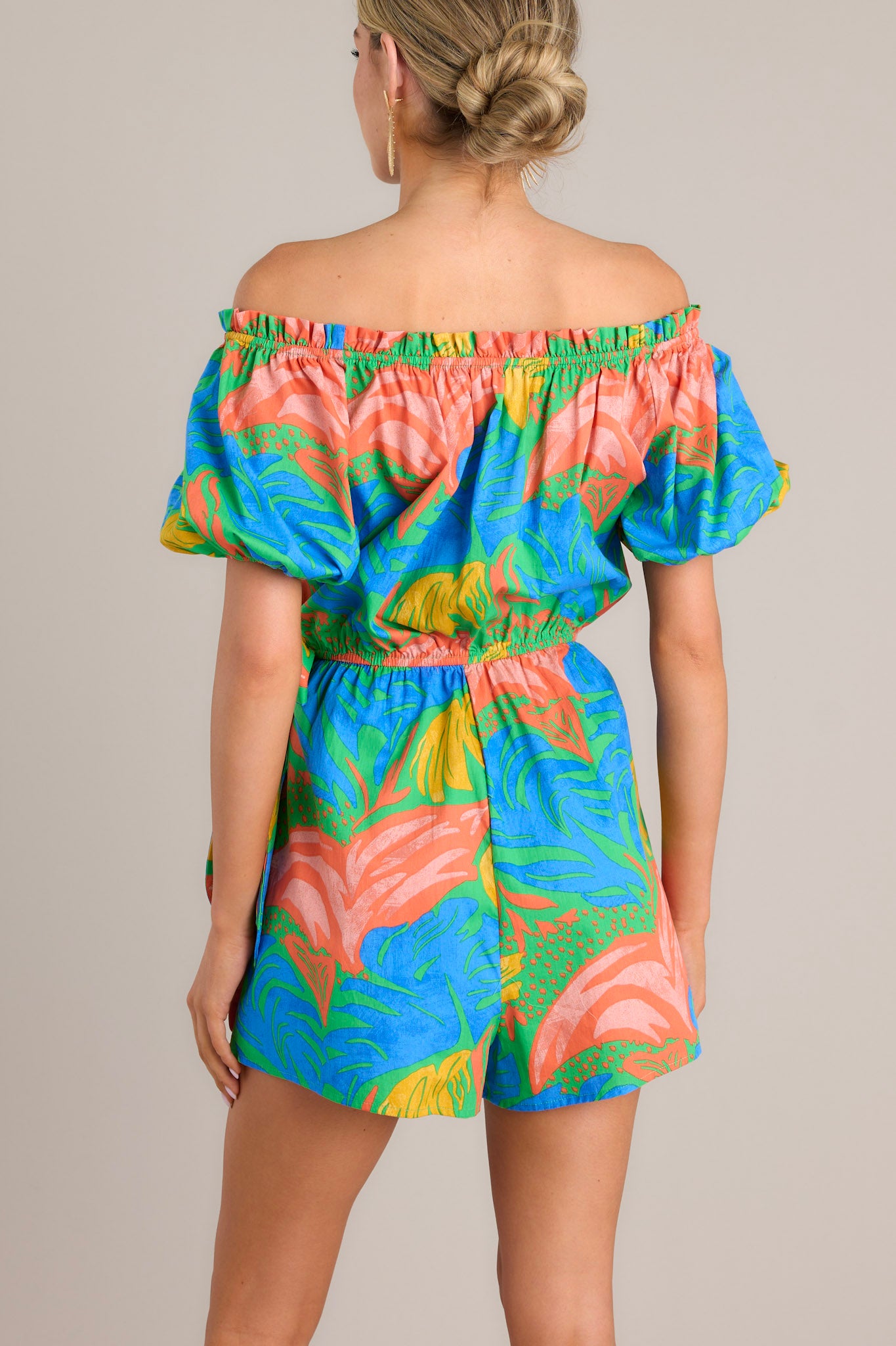 Back view of this romper that features an elastic ruffled strapless neckline, an elastic waistband, a self-tie wrap feature, and elastic cuffed short sleeves.