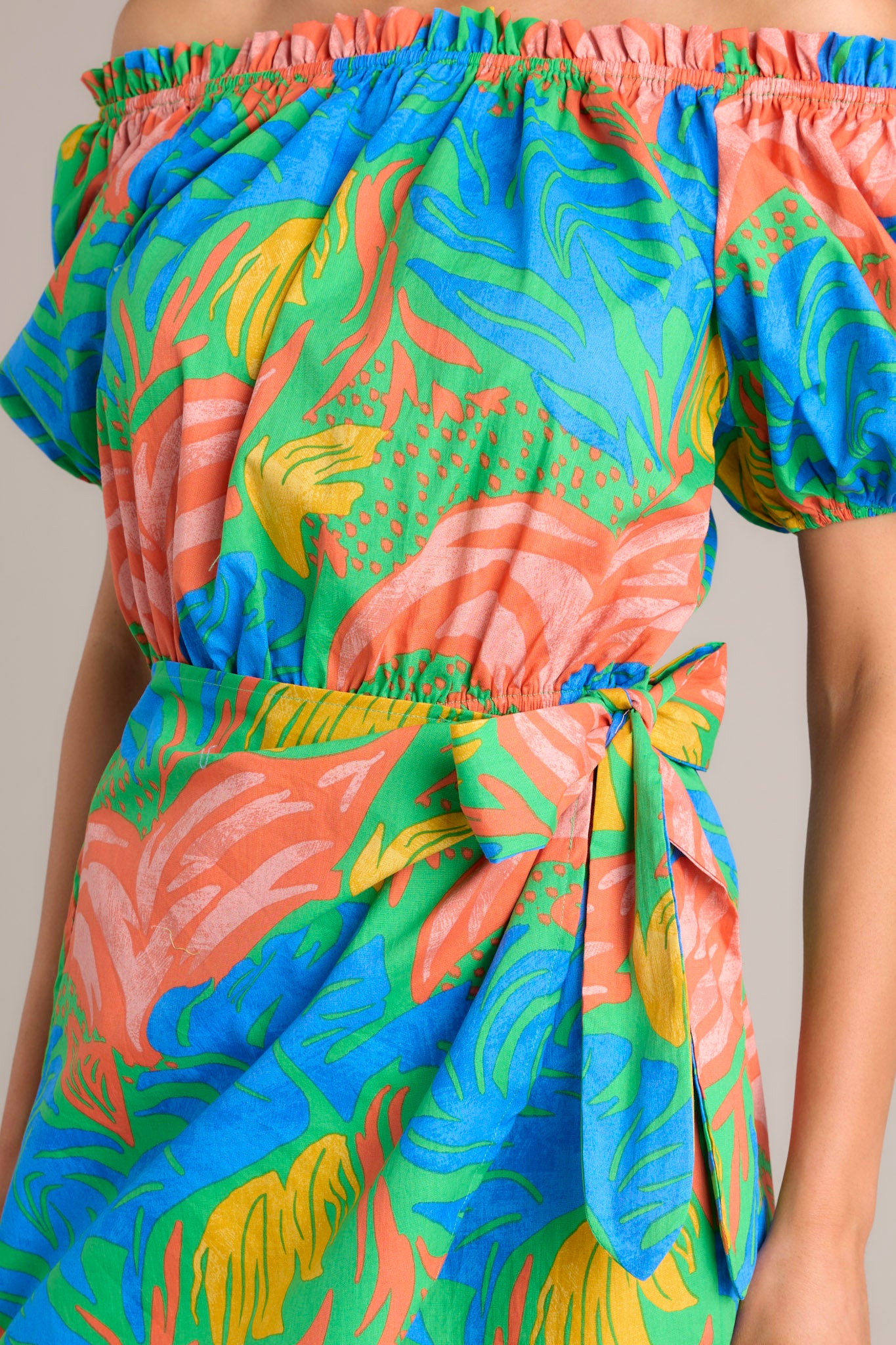 Close up view of this romper that features an elastic ruffled strapless neckline, an elastic waistband, a self-tie wrap feature, and elastic cuffed short sleeves.