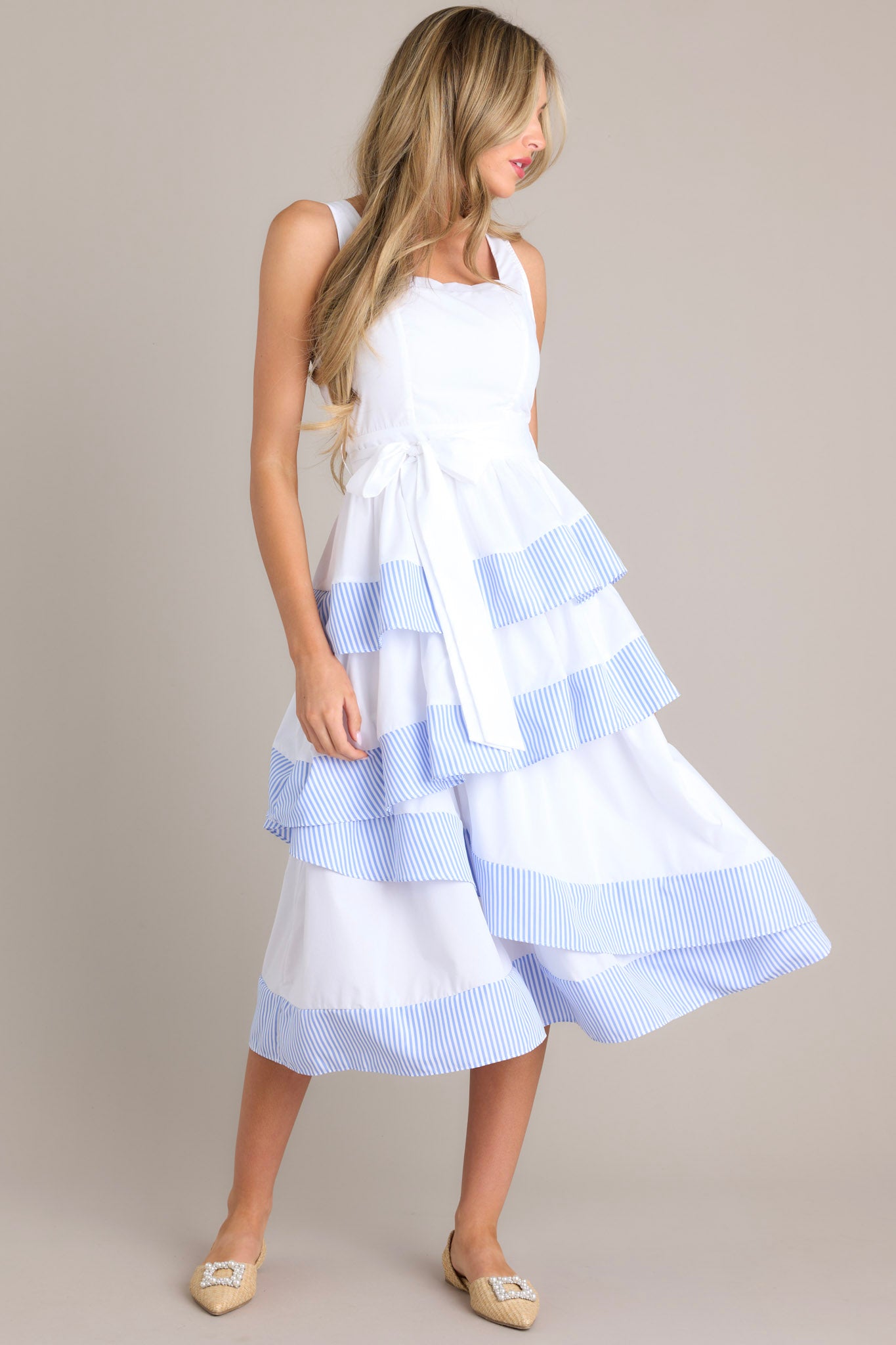 Angled view of this dress that features a square neckline, thick straps, a smocked back insert, a discrete zipper, a self-tie belt, belt loops, and an asymmetrical tiered design.