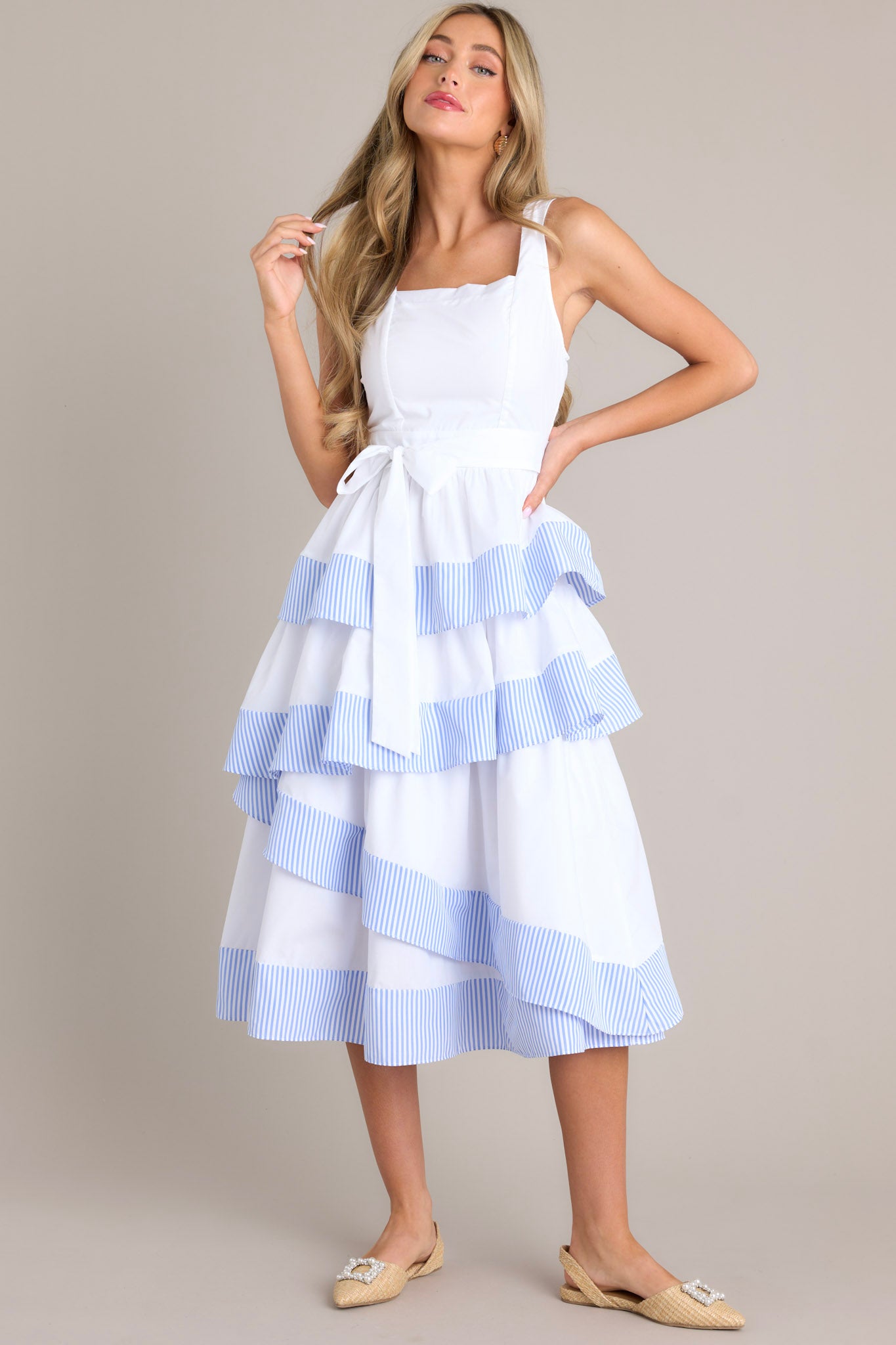 Full front view of this dress that features a square neckline, thick straps, a smocked back insert, a discrete zipper, a self-tie belt, belt loops, and an asymmetrical tiered design.