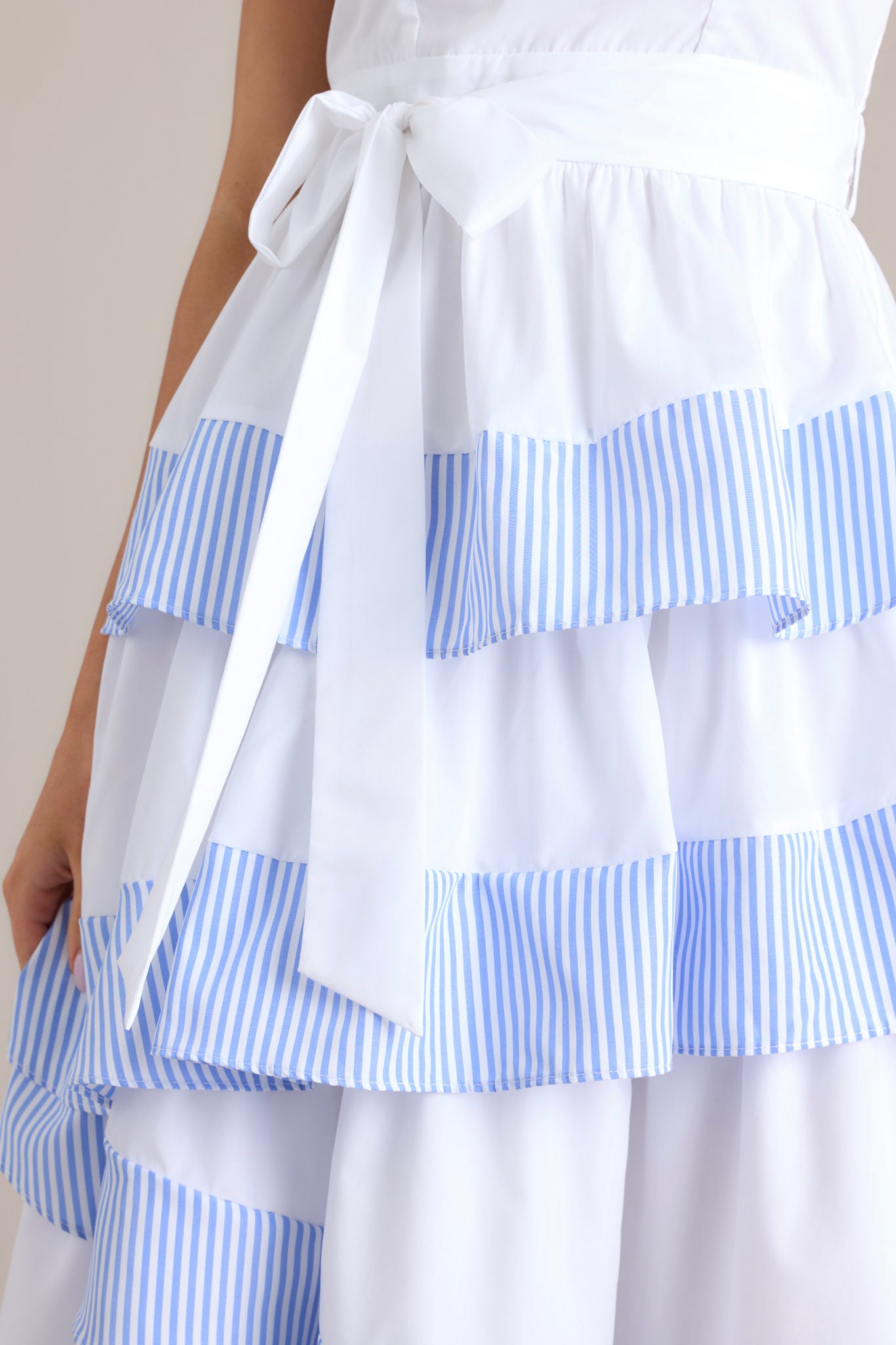 Close up view of this dress that features a square neckline, thick straps, a smocked back insert, a discrete zipper, a self-tie belt, belt loops, and an asymmetrical tiered design.