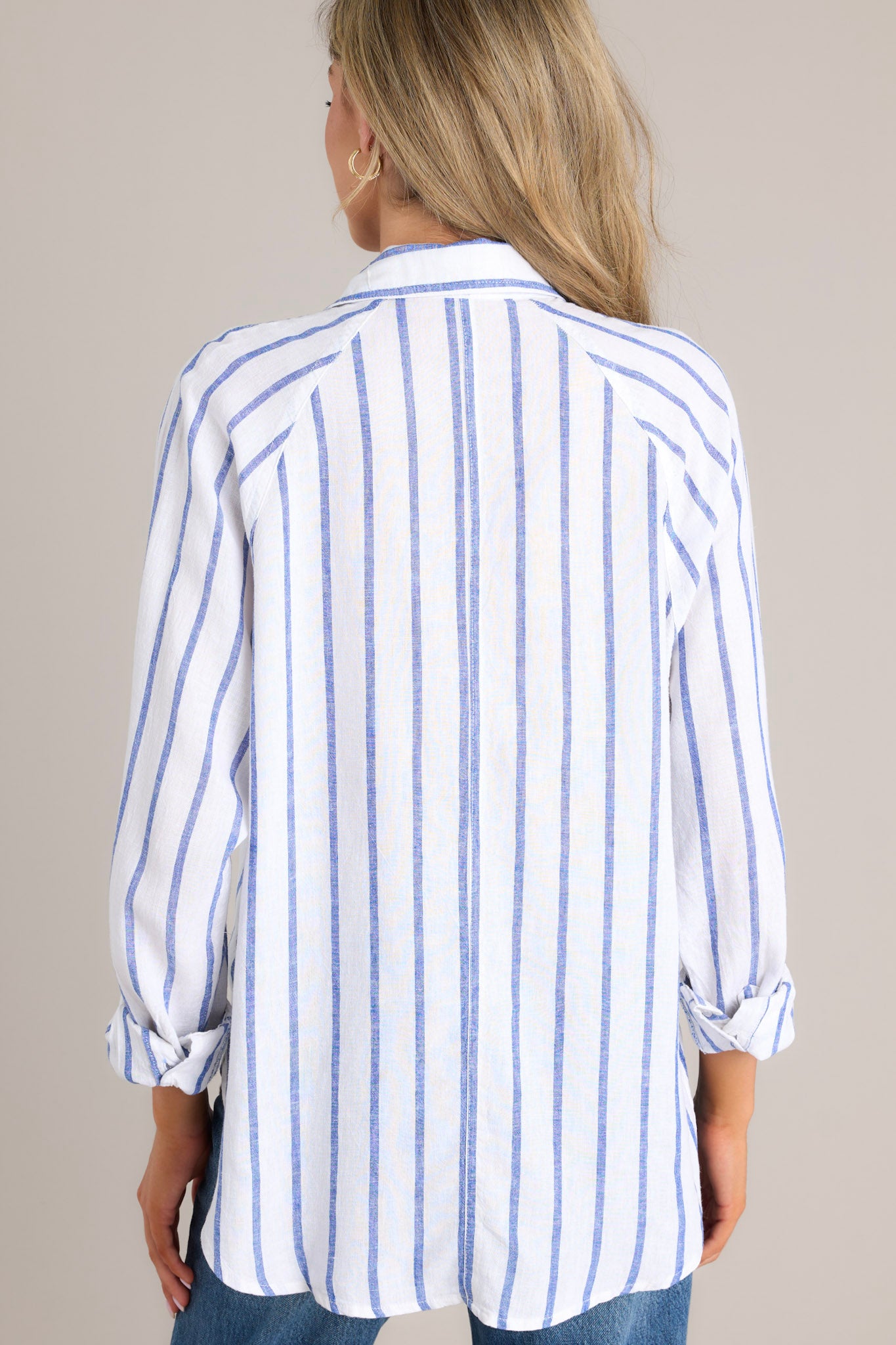 Back view of this stripe top that features a collared neckline, a functional button front, a breast pocket, button cuffed long sleeves, and a split high low hemline.