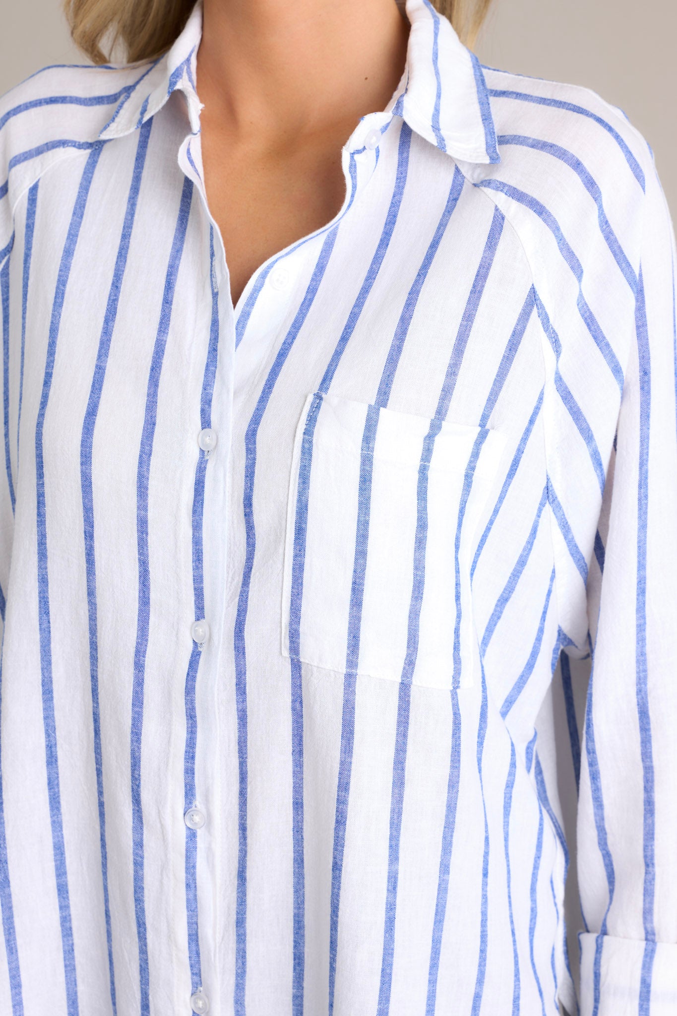 Close up view of the material of this stripe top that features a collared neckline, a functional button front, a breast pocket, button cuffed long sleeves, and a split high low hemline.