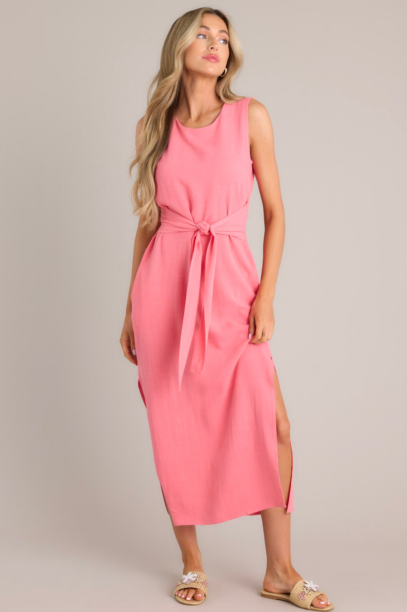 Front  view of this coral dress that features a rounded neckline, a back keyhole cutout with functional button, a smocked back insert, a self-tie waist feature, functional hip pockets, and side slits.