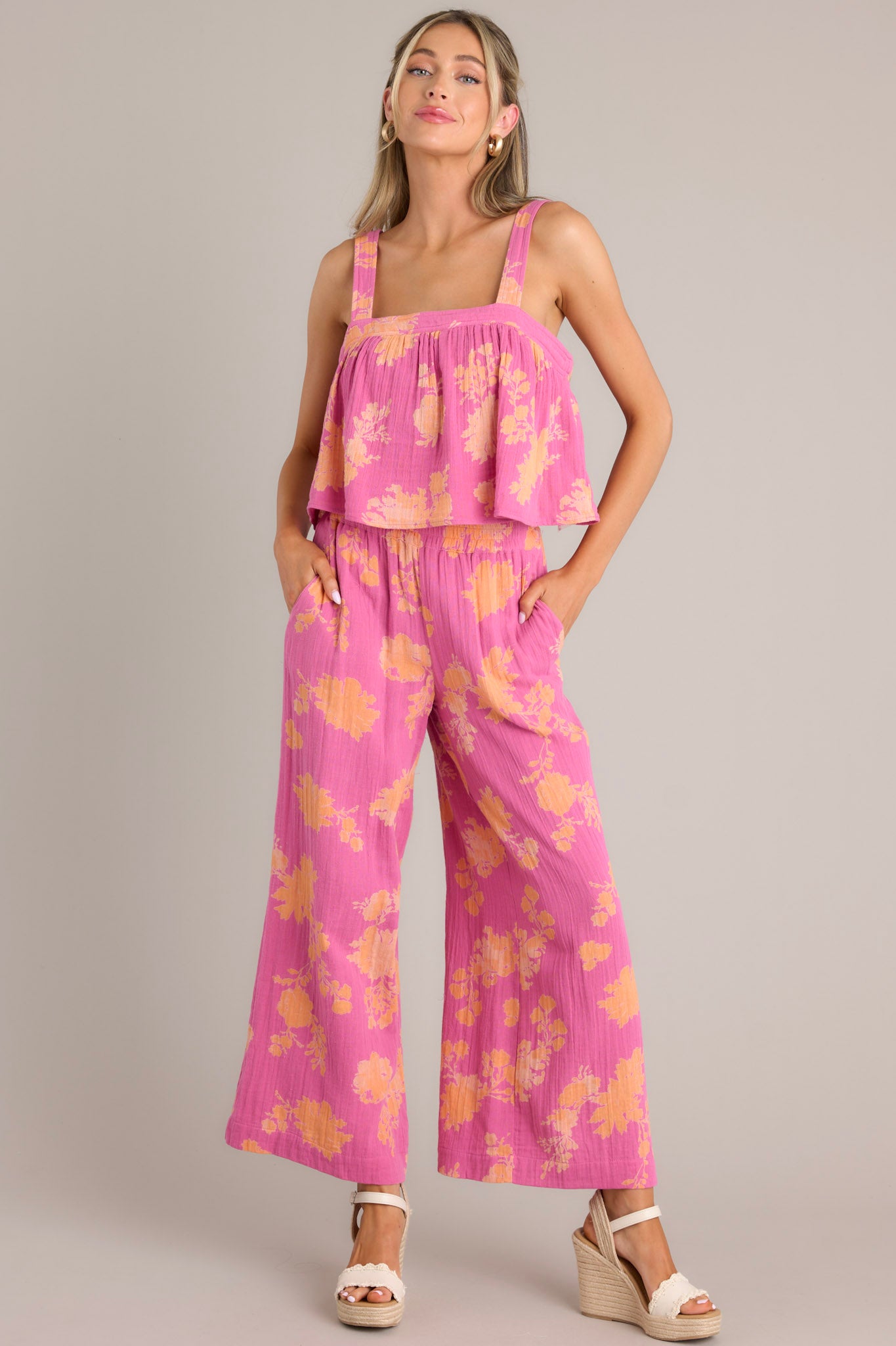 Angled full body view of these pink floral pants that feature a high waisted design, a thick elastic waistband, functional hip pockets, and a wide leg.