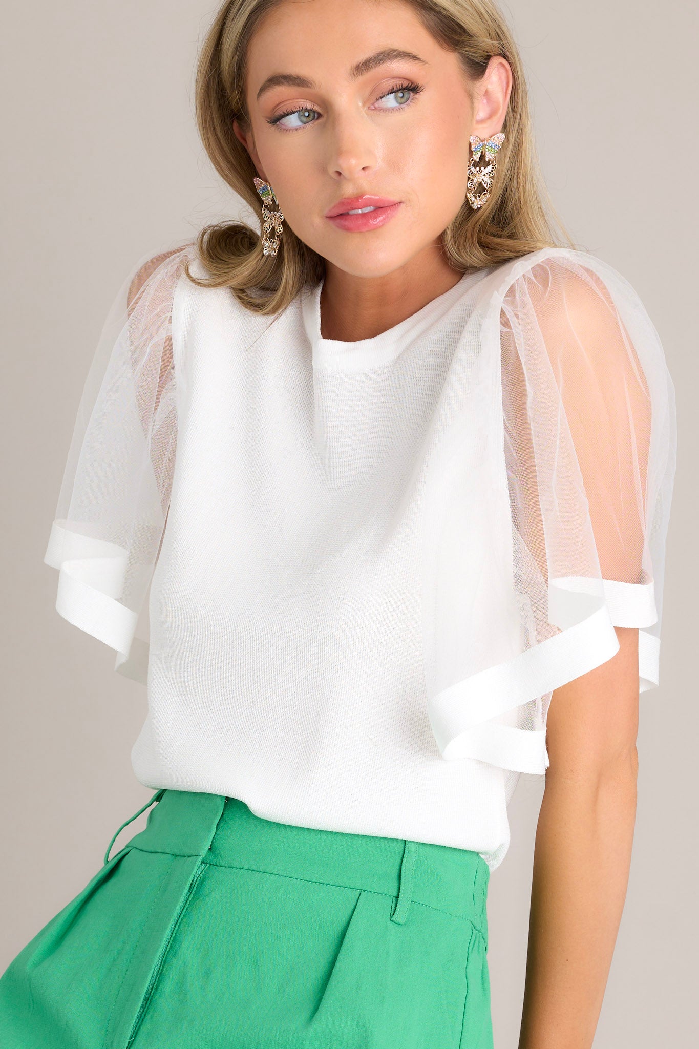 Angled close up view of this white top features a crew neckline, a soft stretchy fabric, and sheer butterfly short sleeves.