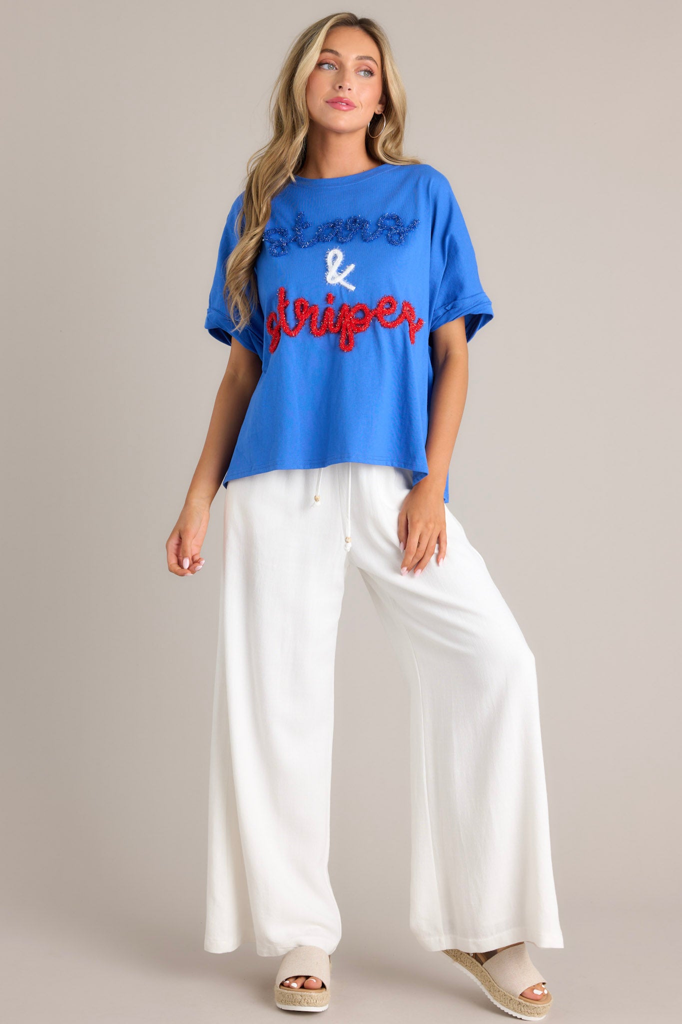 Angled full body view of this blue top that features a crew neckline, textured 3D writing, an extremely oversized fit, and cuffed wide short sleeves.