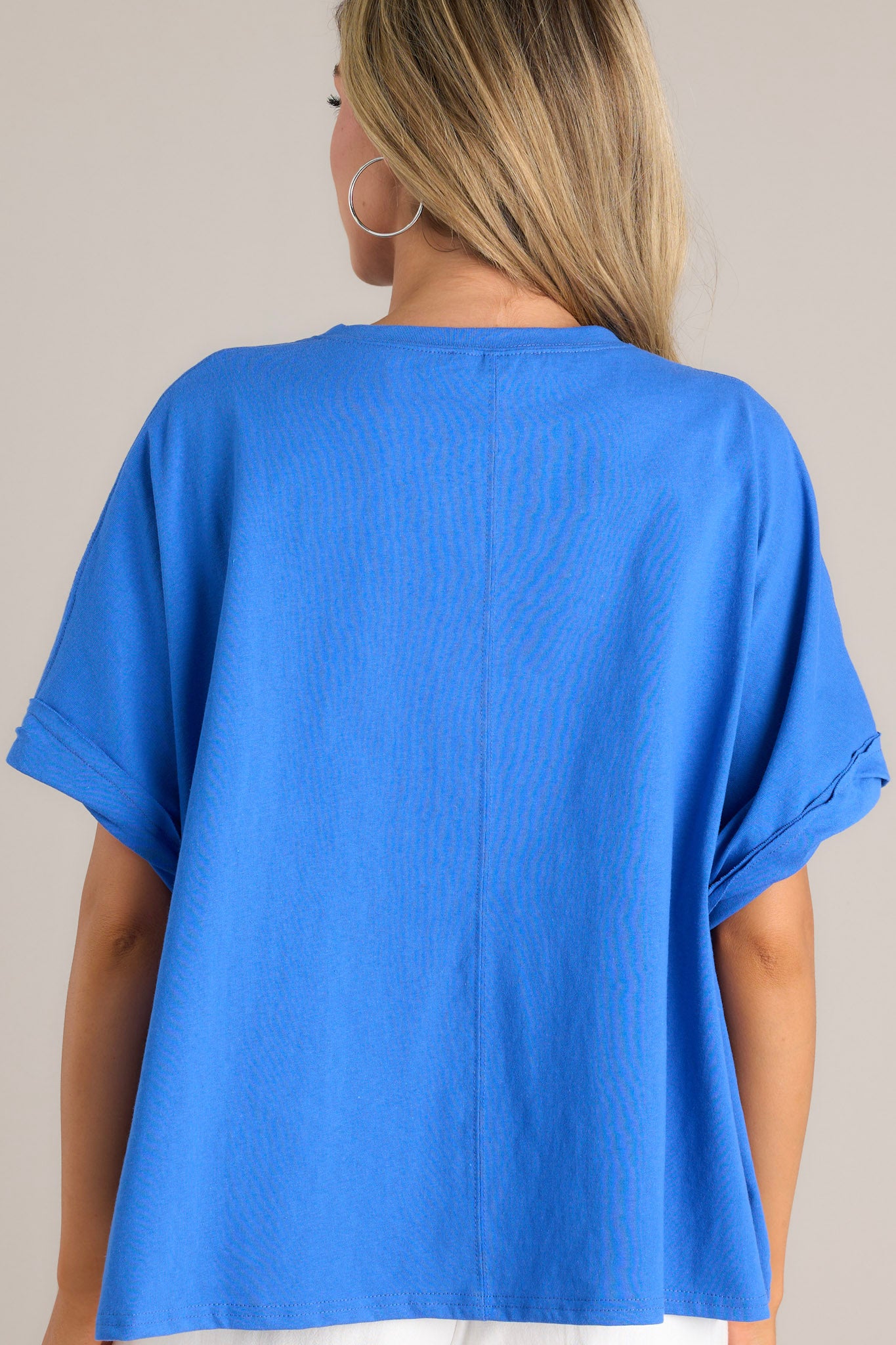 Back view of this blue top that features a crew neckline, textured 3D writing, an extremely oversized fit, and cuffed wide short sleeves.