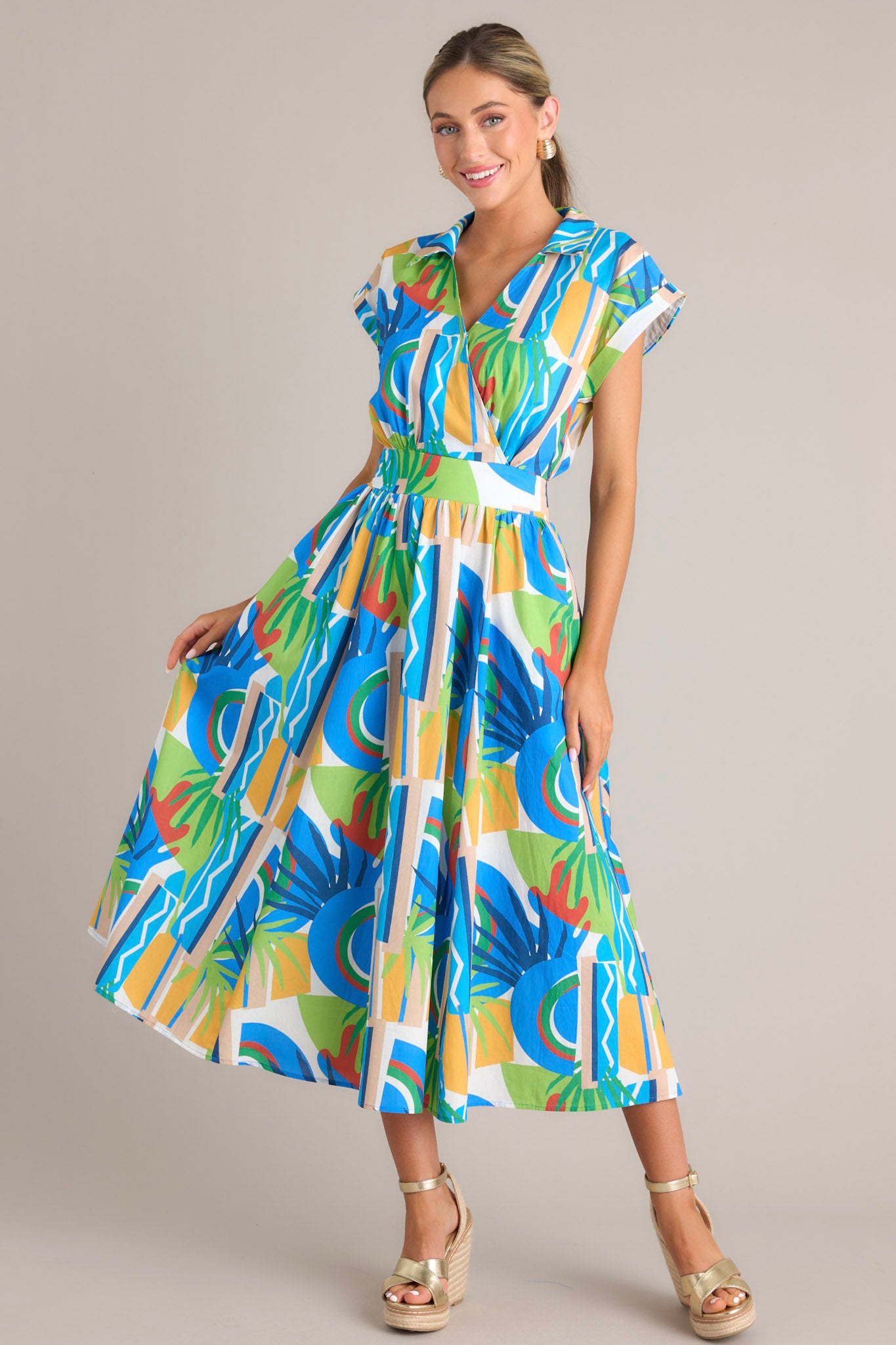 Action shot of a colorful wrap dress with an abstract blue, green, yellow, and red pattern, featuring a cinched waist and cap sleeves, highlighting the flow and movement of the dress.