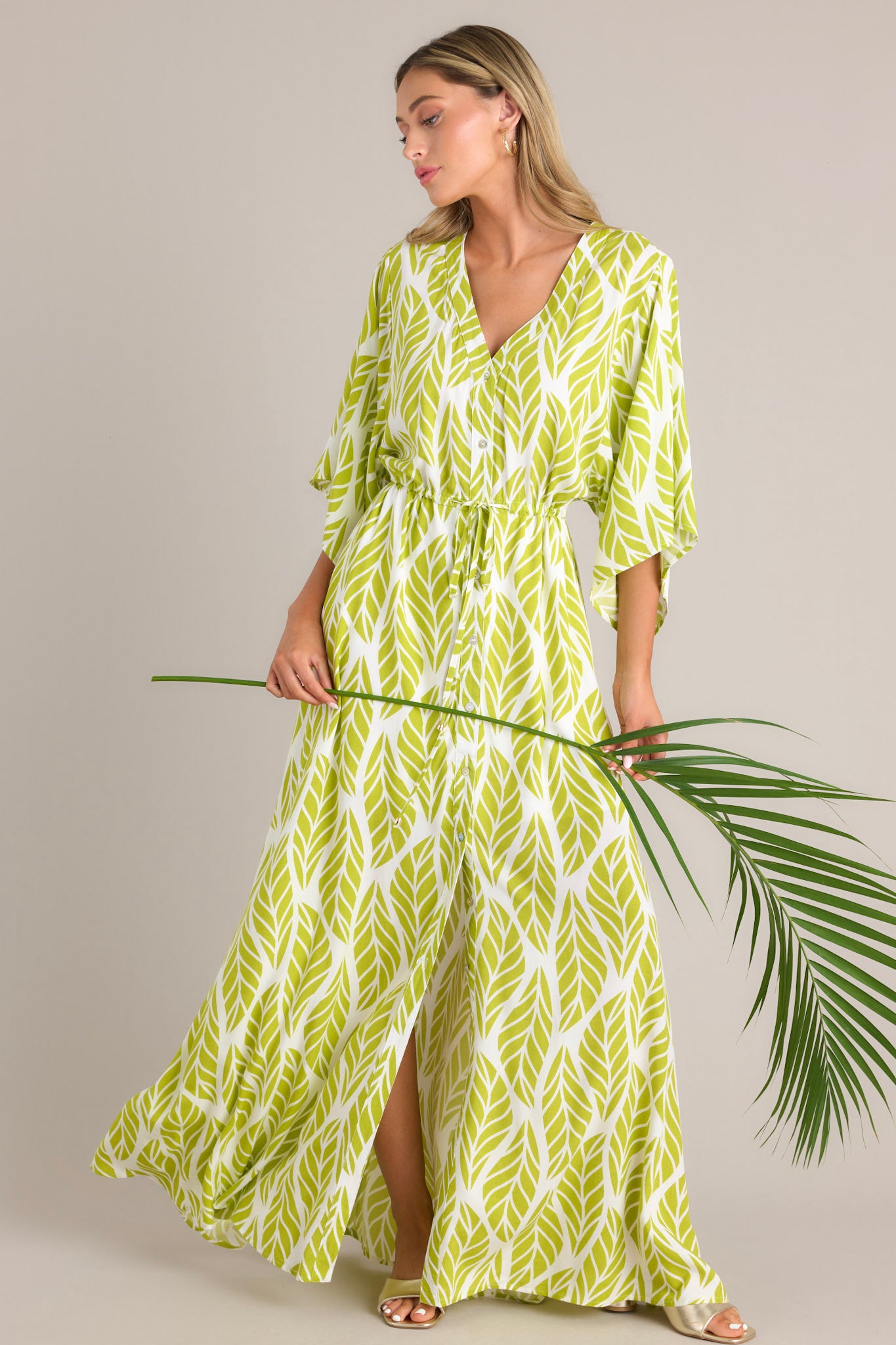 Angled view of this lime green maxi dress that features a v-neckline, a functional button front, a self-tie drawstring waist, a flowing silhouette, and flowing half sleeves.