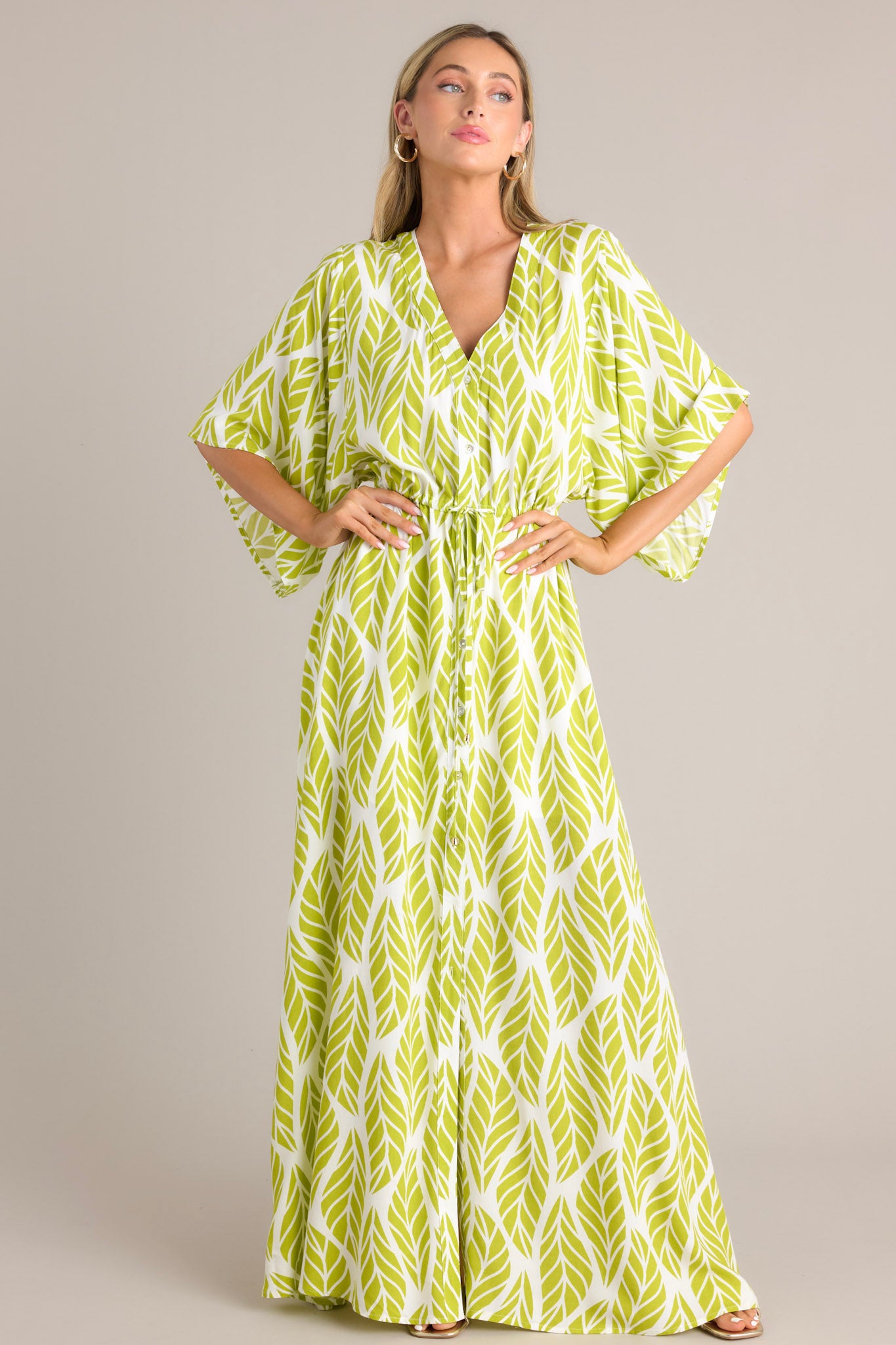 Full body view of this lime green maxi dress that features a v-neckline, a functional button front, a self-tie drawstring waist, a flowing silhouette, and flowing half sleeves.