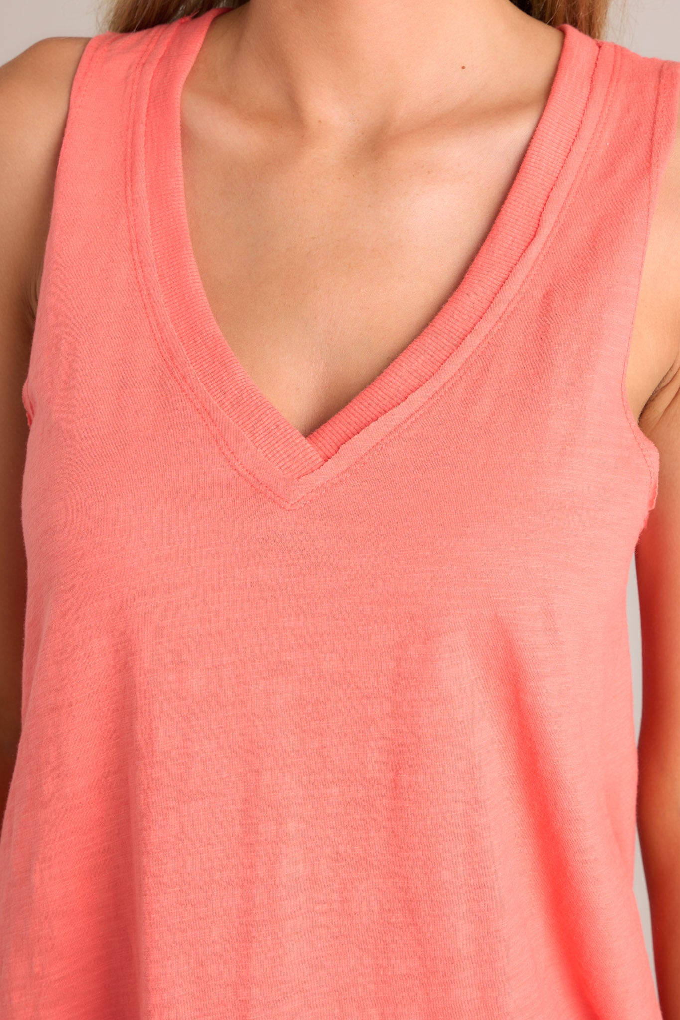 Close up view of this tank that features a v-neckline, a sleeveless design, a bold color, and a scoop hemline.