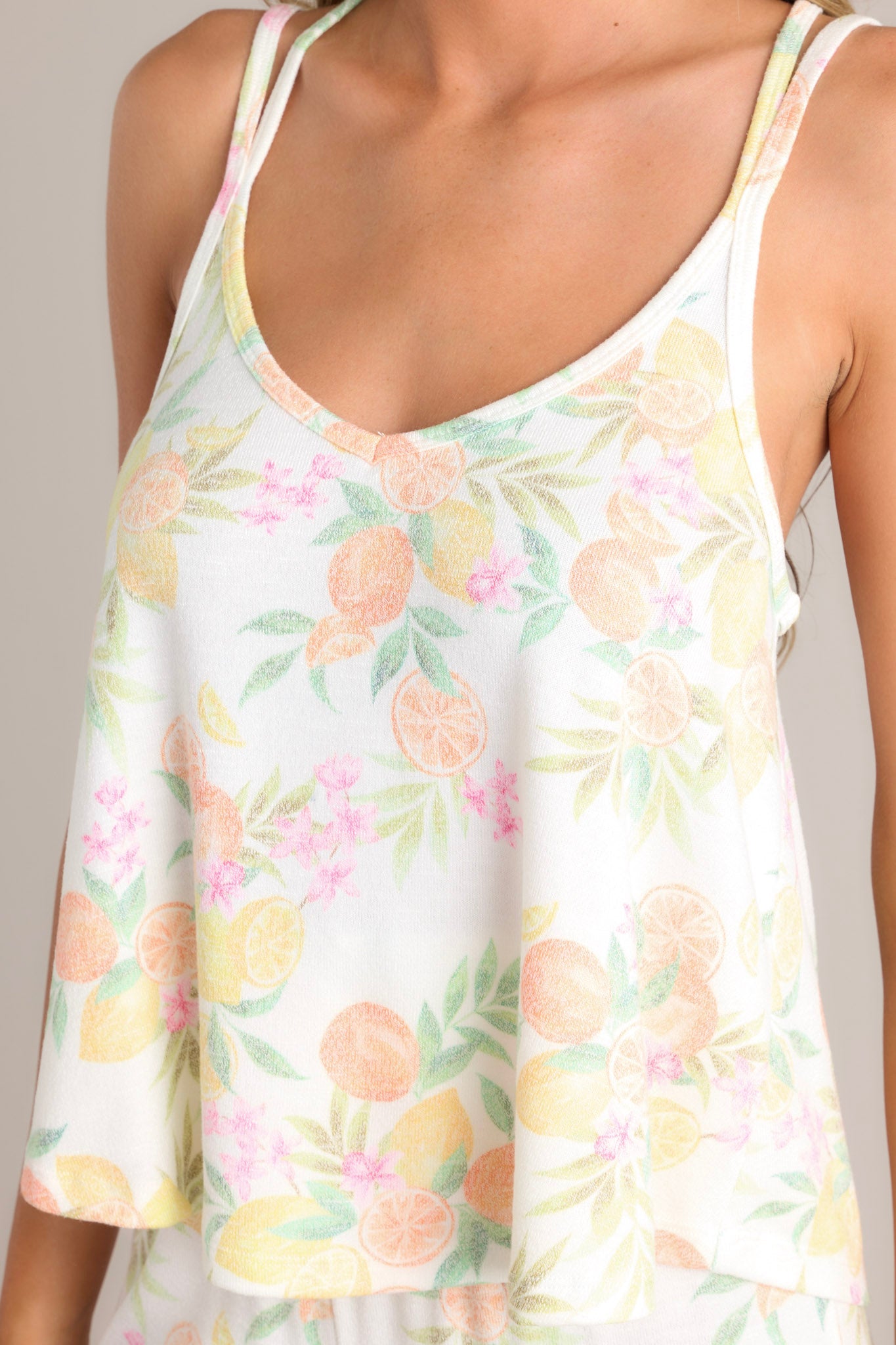 Close up view of this white citrus tank that features a v-neckline, thin double straps, a relaxed fit, and a soft knit material.