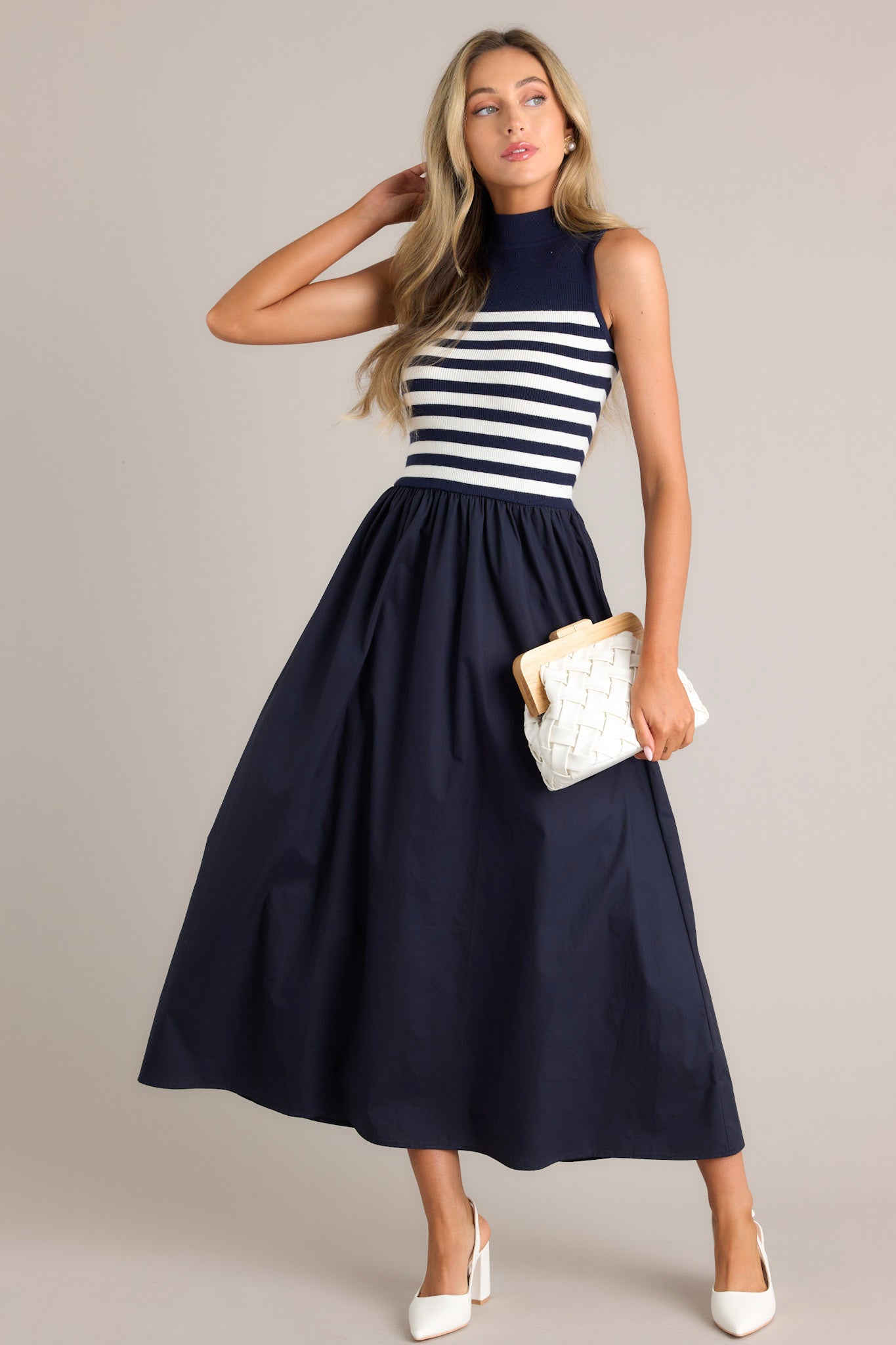 Angled full body view of this navy stripe maxi dress that features a high neckline, a striped sweater bodice, and a flowy skirt.