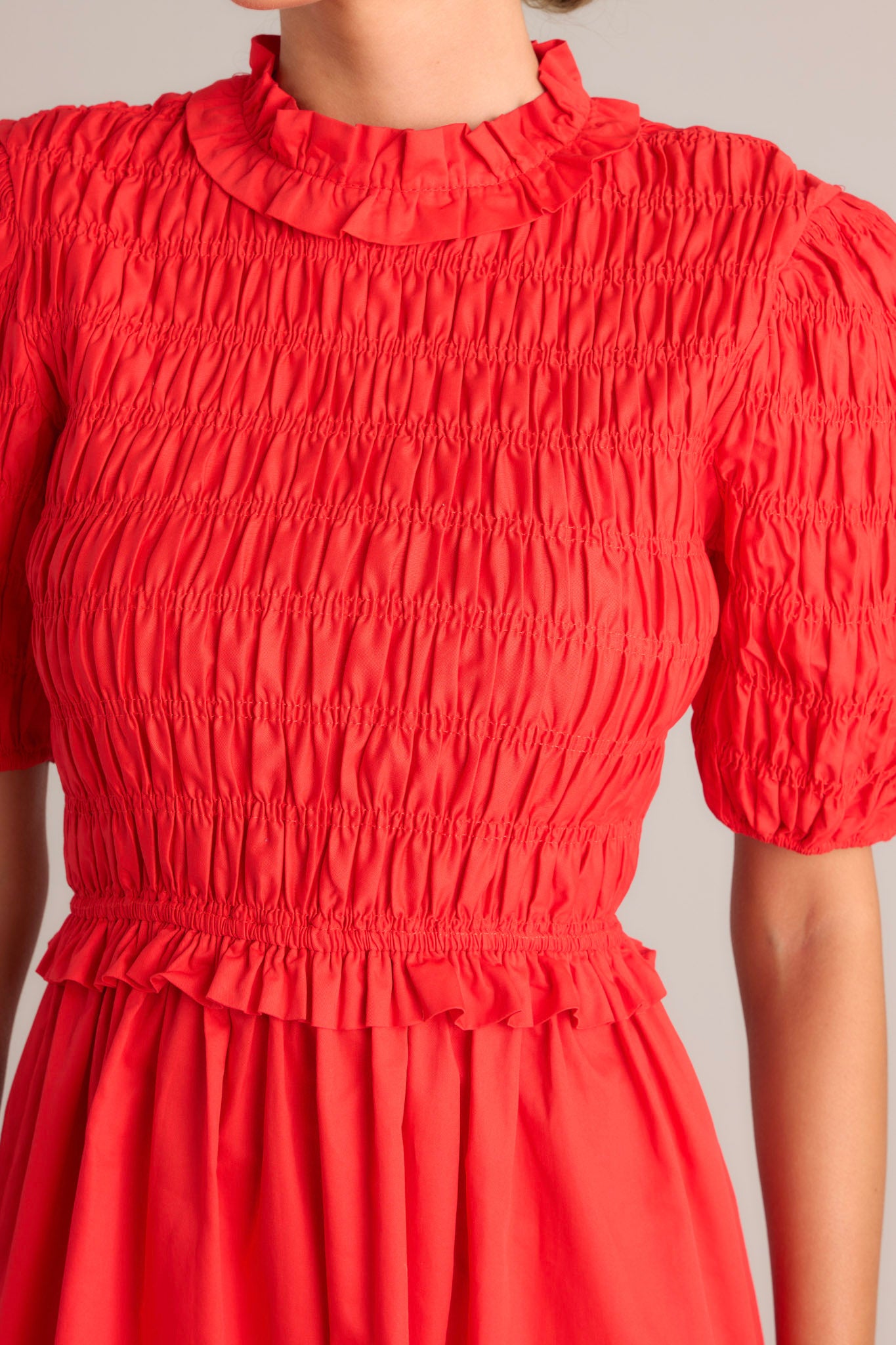 Close up view of this red midi dress that features high ruffled neckline, a keyhole with button closure, a fully smocked bodice, a tiered design, a fully smocked elastic cuffed half sleeves.