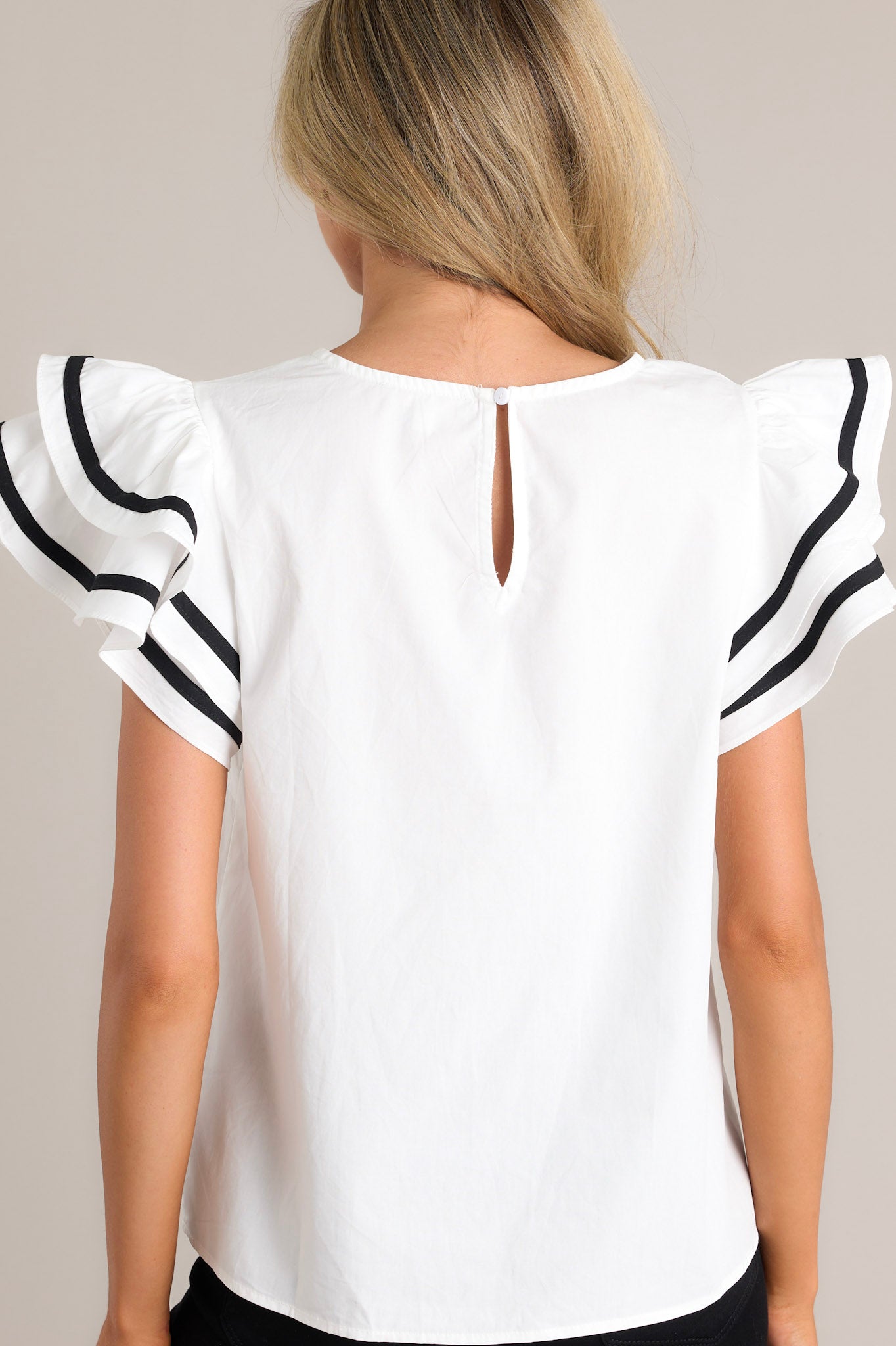 Back view this white top featuring a crew neckline, a keyhole cutout with a button closure, a relaxed fit, and short flutter sleeves with contrasting stripes.