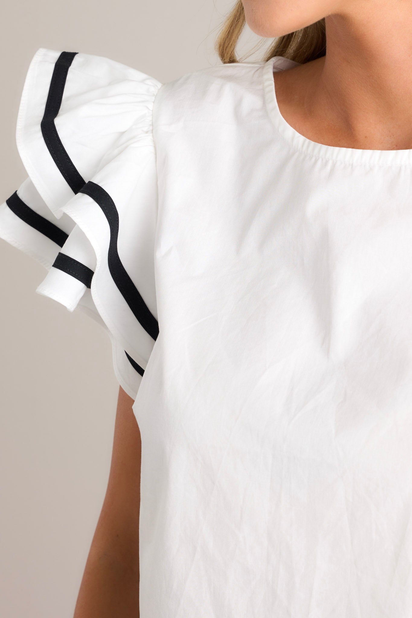 Close up of this white top featuring a crew neckline, a keyhole cutout with a button closure, a relaxed fit, and short flutter sleeves with contrasting stripes.