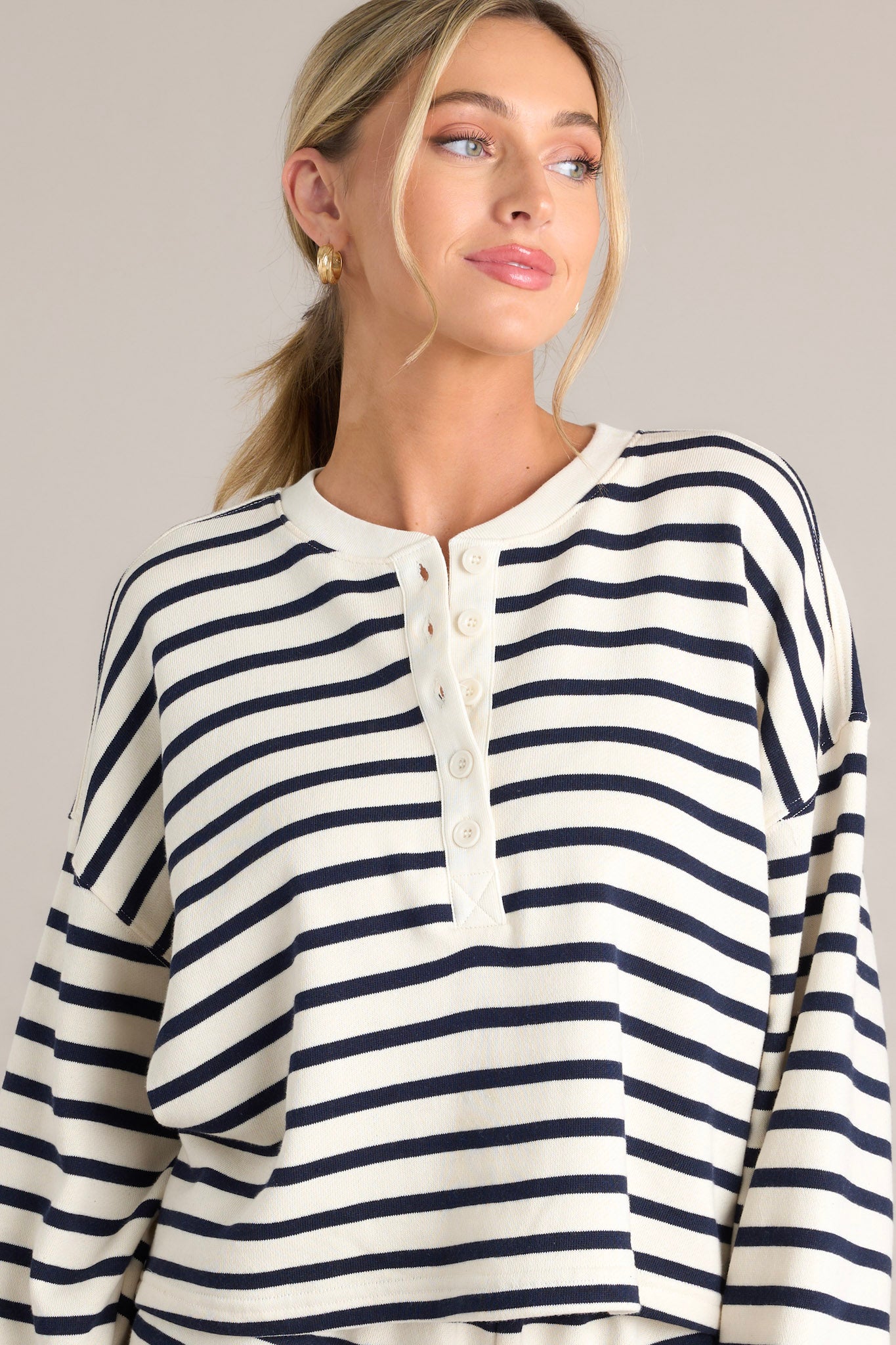 Angled front view this navy stripe pullover that features a crew neckline, a functional button front, classic stripes, and ribbed cuffed long sleeves.